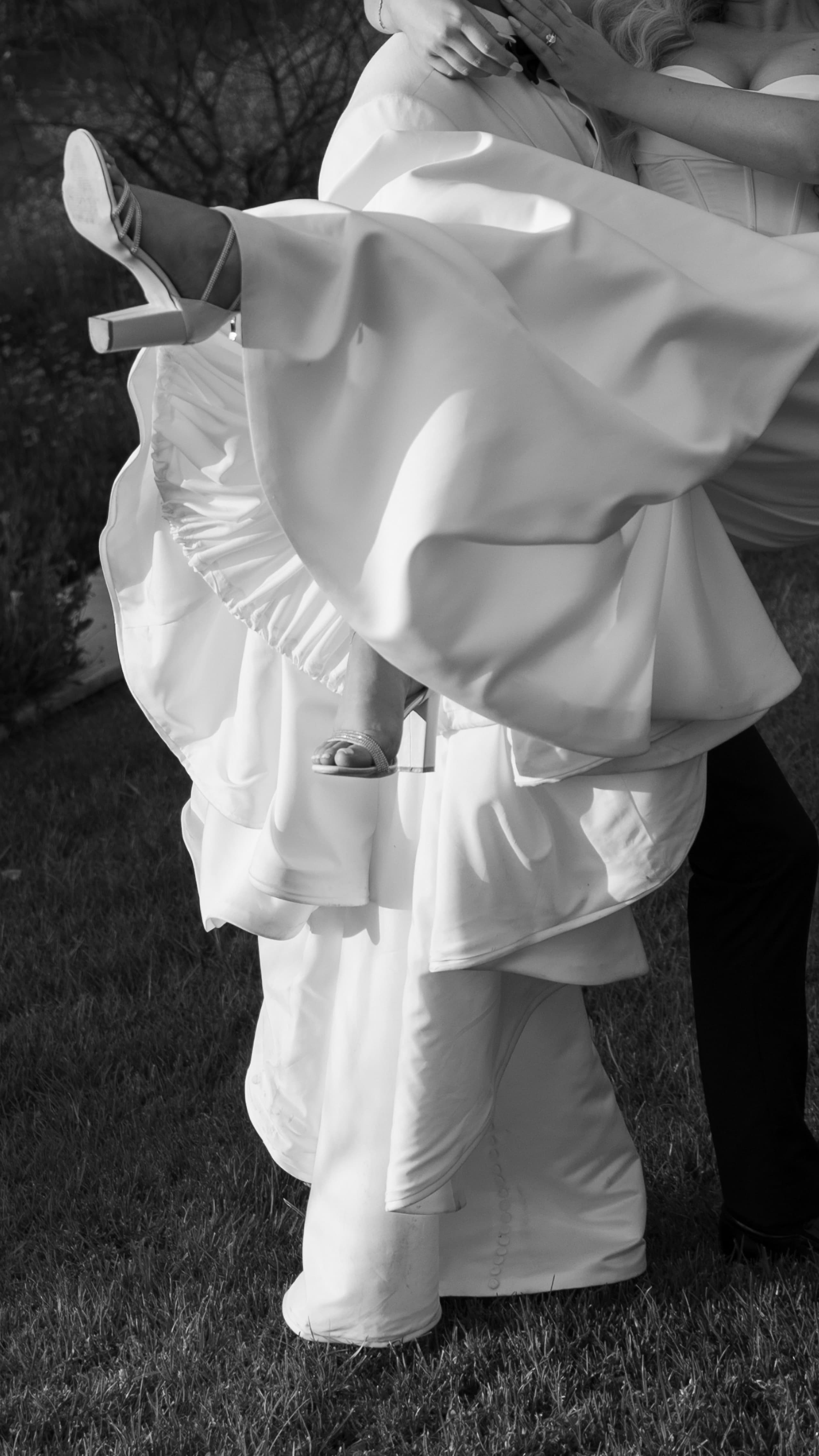 A bride in a flowing white gown is being lifted by her groom outdoors