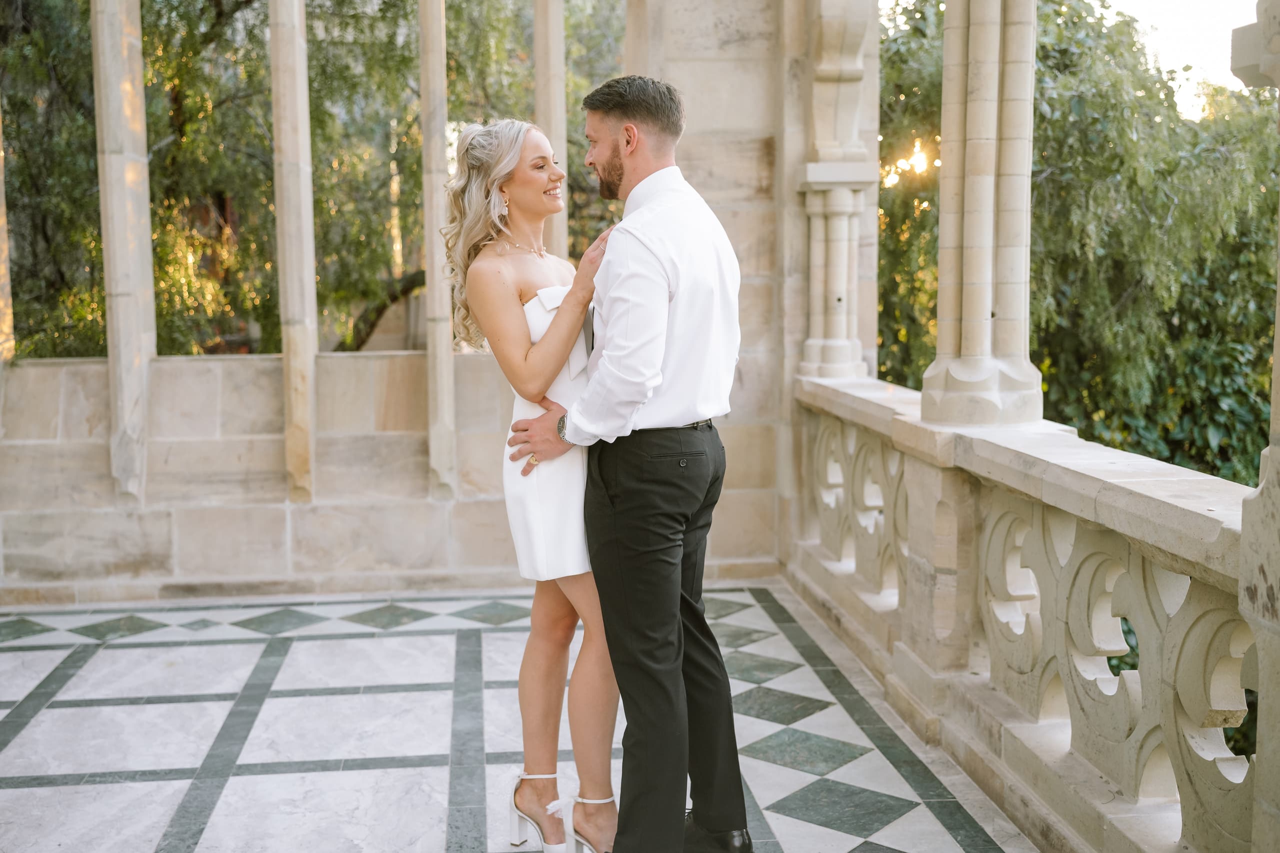 A bride and groom embrace affectionately on a stone balcony during their luxury wedding celebration