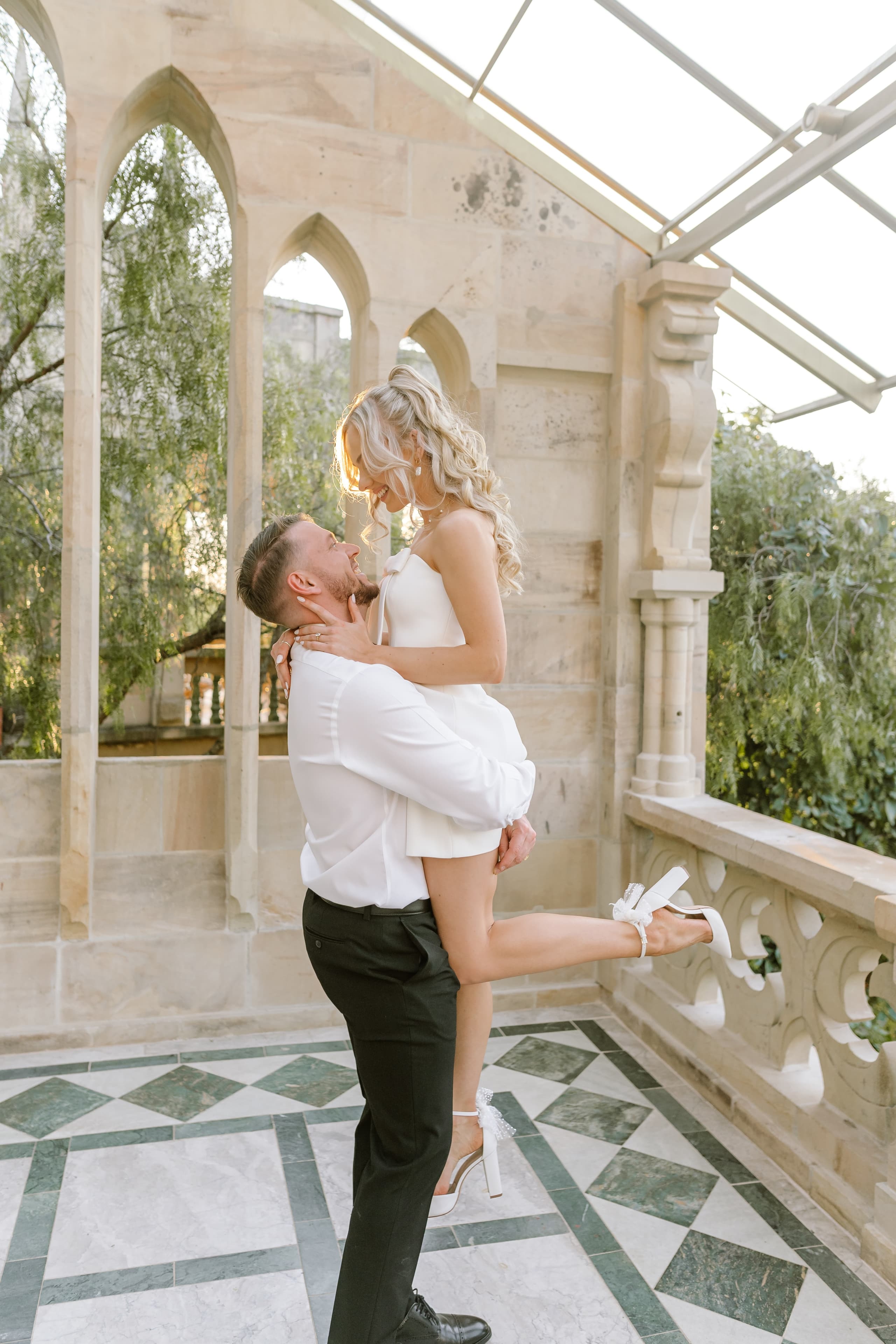 A groom lifts his bride in a romantic embrace at a sunlit stone wedding venue
