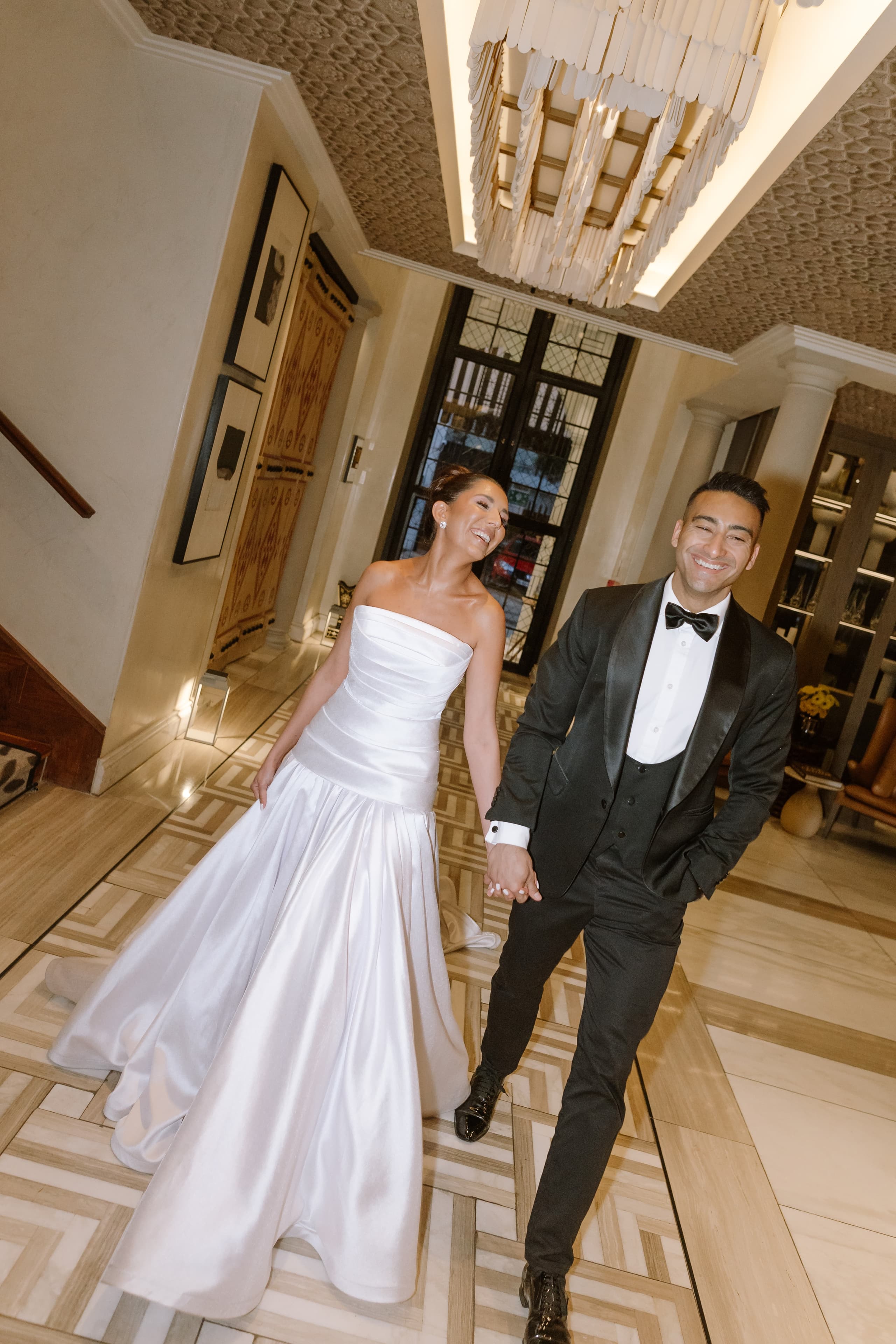 A joyful bride and groom walk hand in hand through a luxurious hotel lobby
