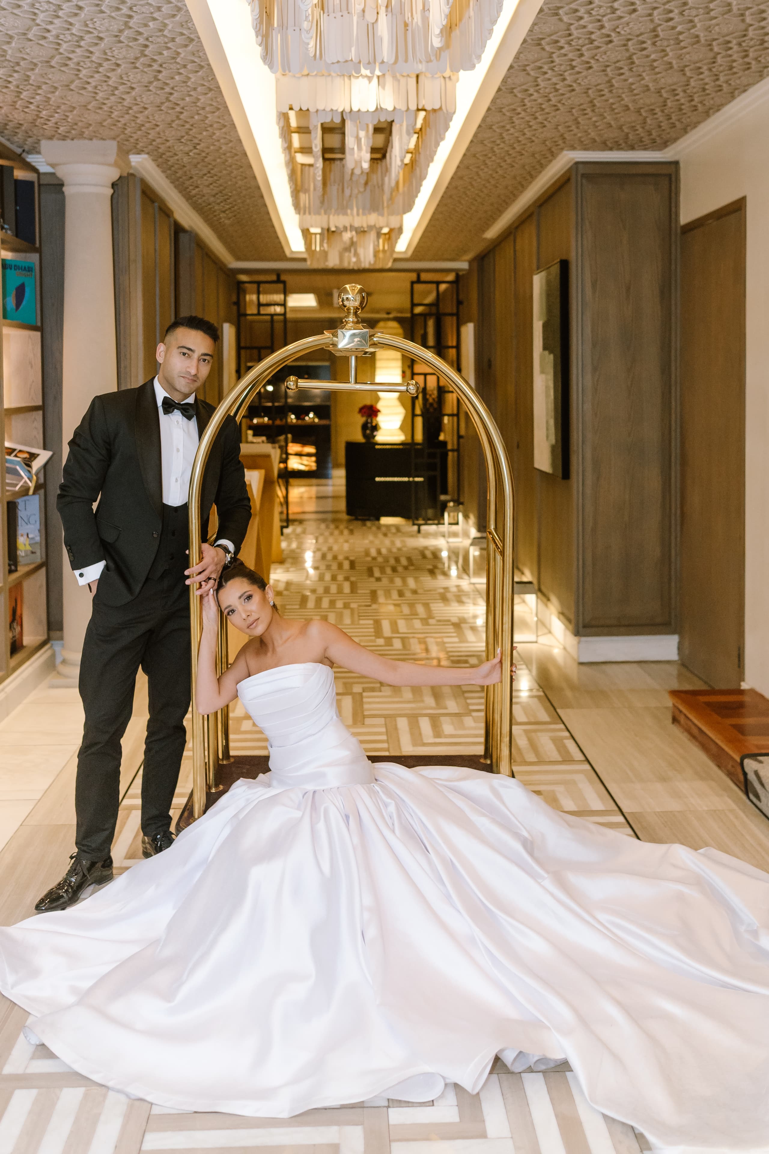 A bride in a white strapless gown poses beside a groom in a tuxedo