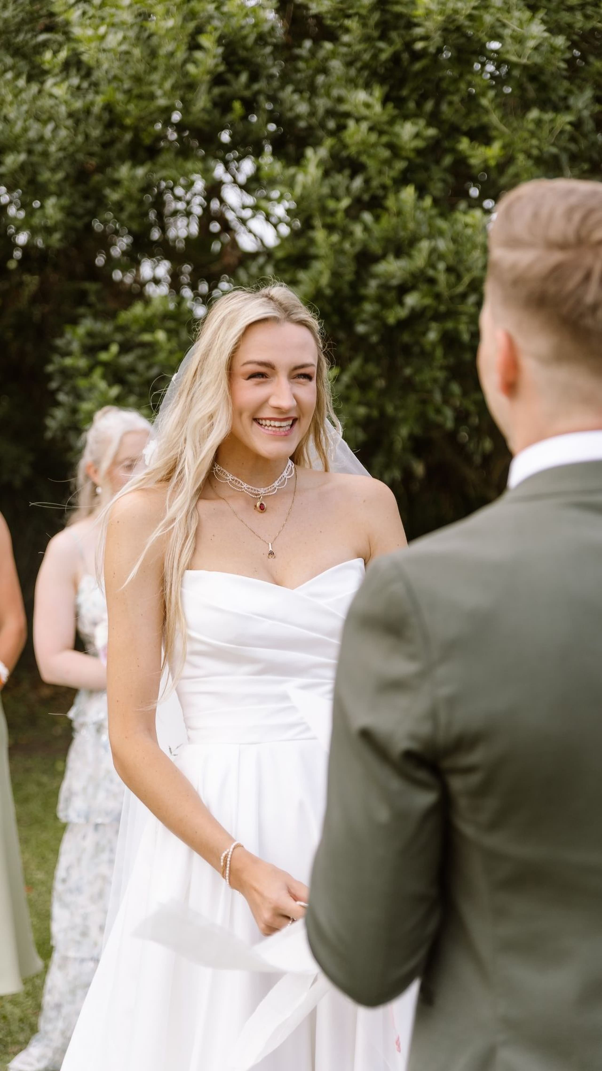 A smiling blonde bride in a white strapless gown looking at her groom during an outdoor wedding ceremony in South Africa