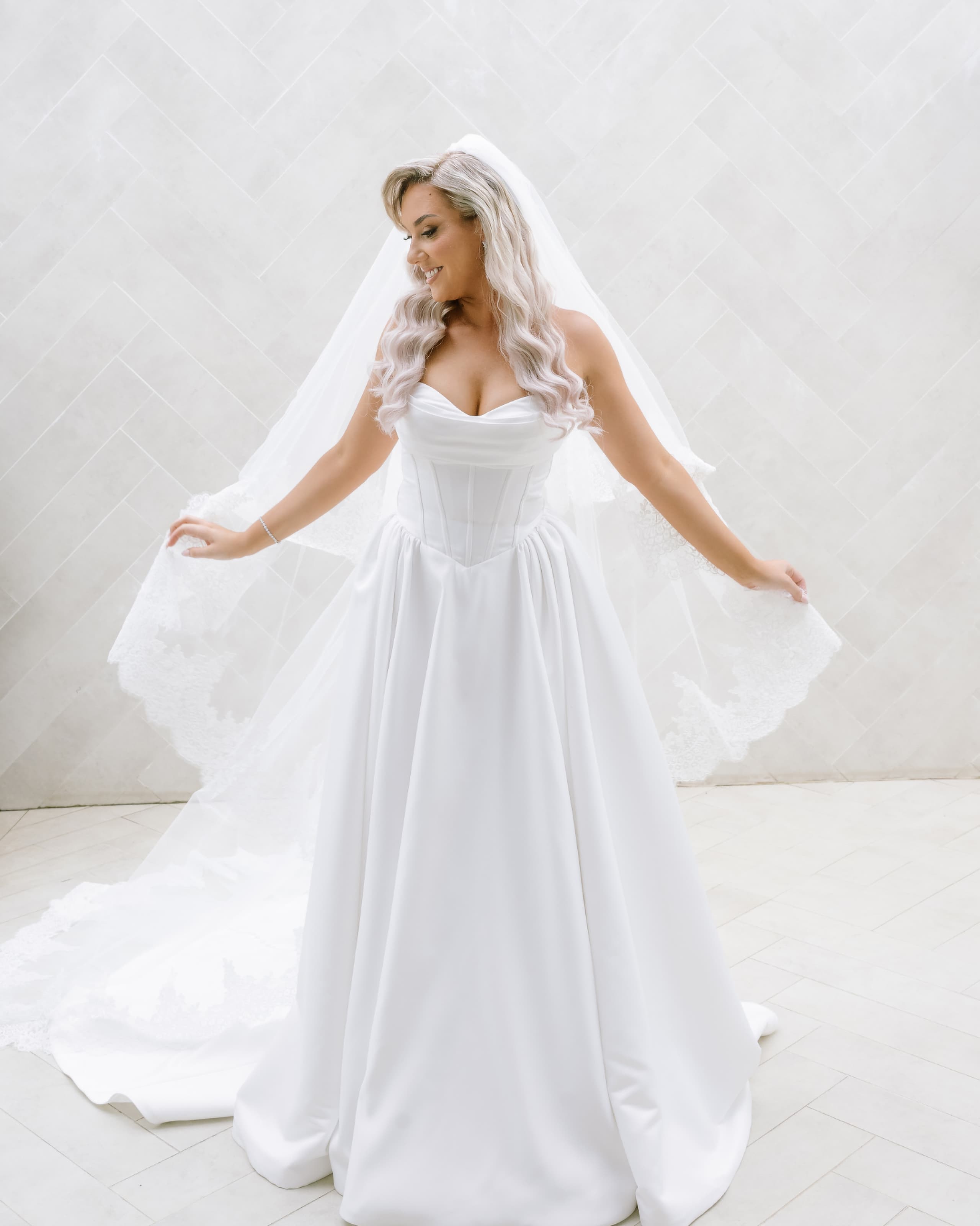A smiling bride with long wavy hair wearing a strapless corset wedding dress and veil