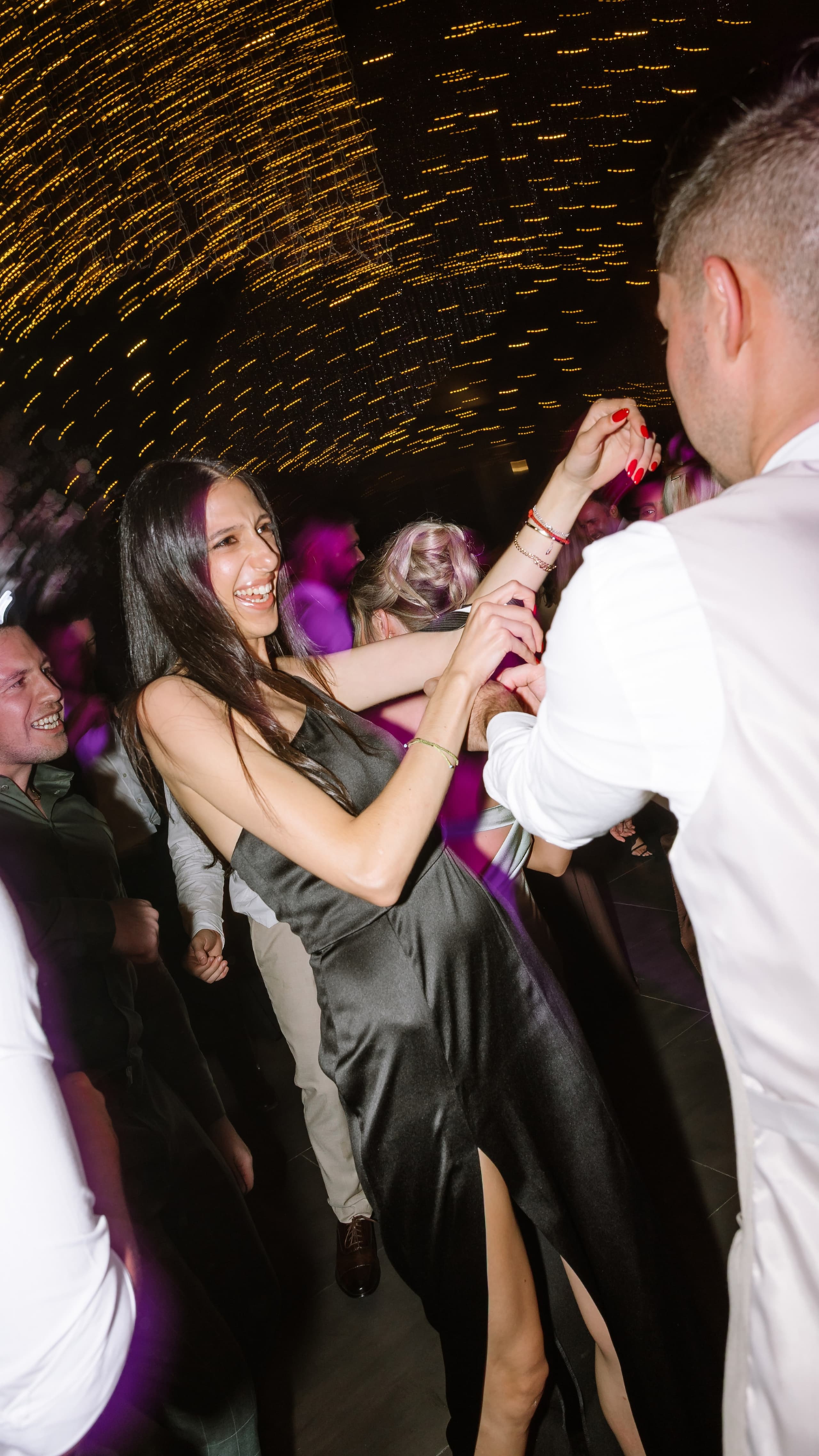 A woman in a black satin dress laughs while dancing with a man at a wedding