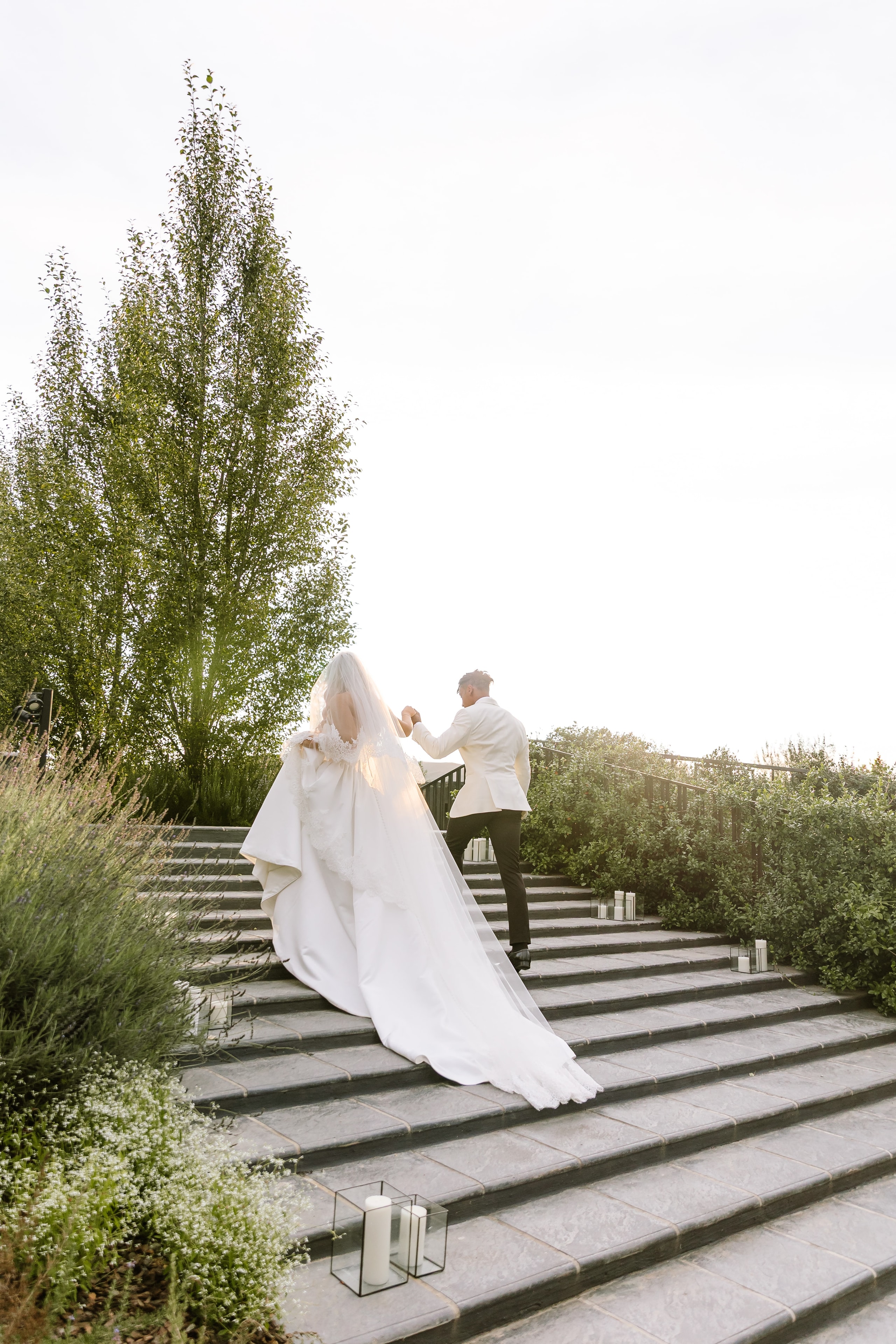 Newlywed couple walking up stone outdoor steps hand in hand at twilight