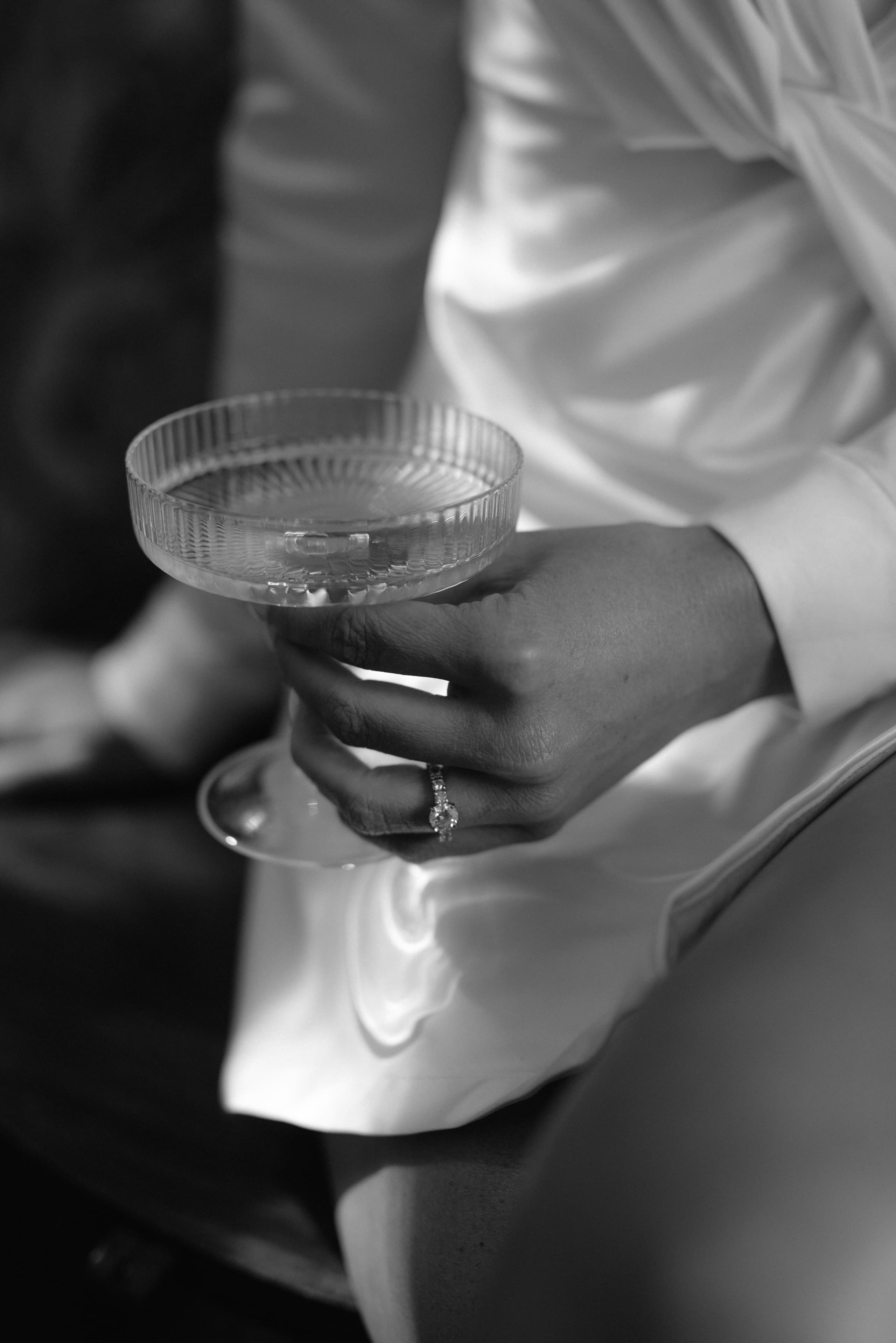 A bride wearing a diamond engagement ring holds an elegant ribbed champagne coupe glass
