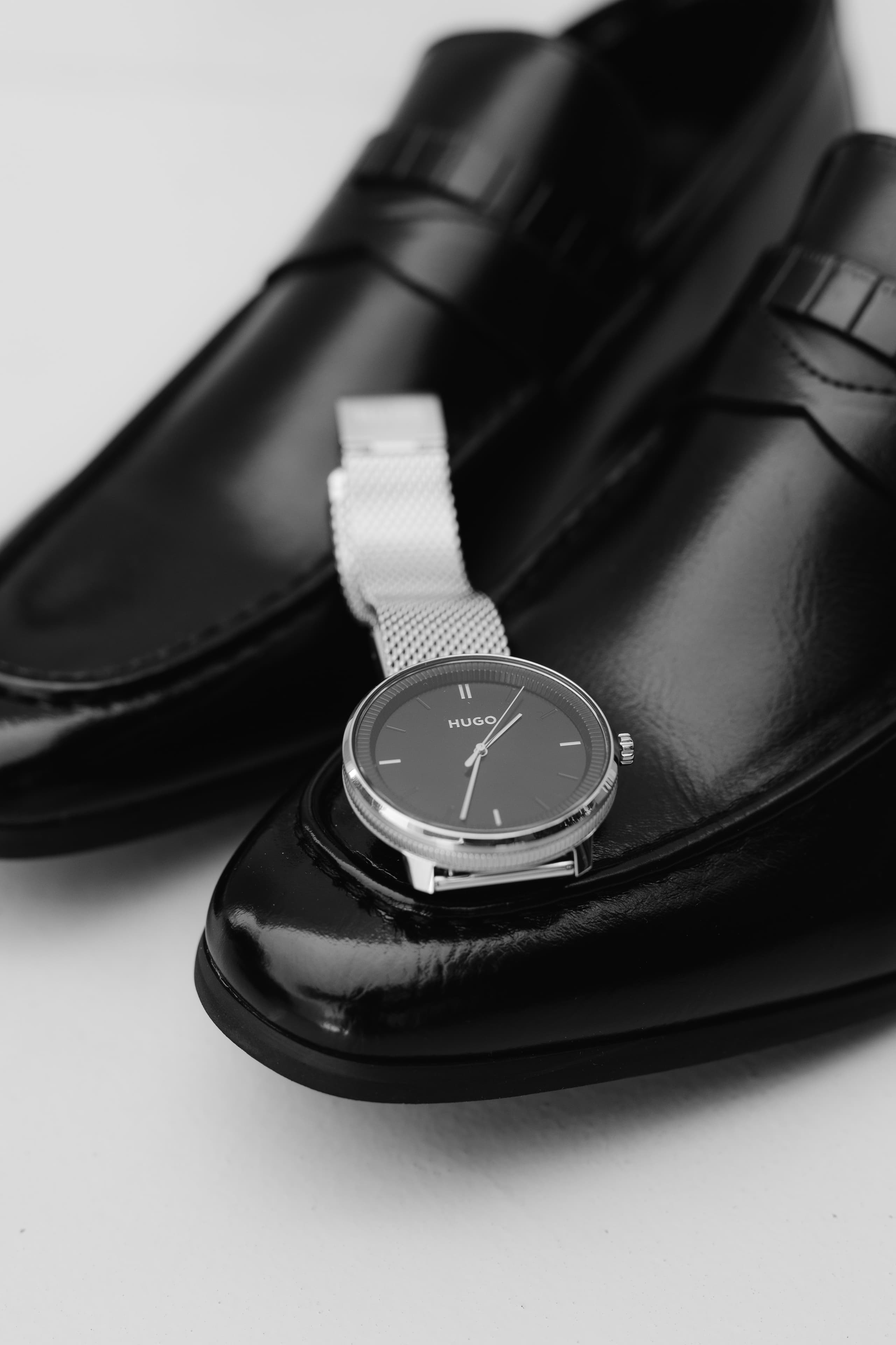 A sleek silver HUGO wristwatch resting elegantly on a polished black leather loafer shoe