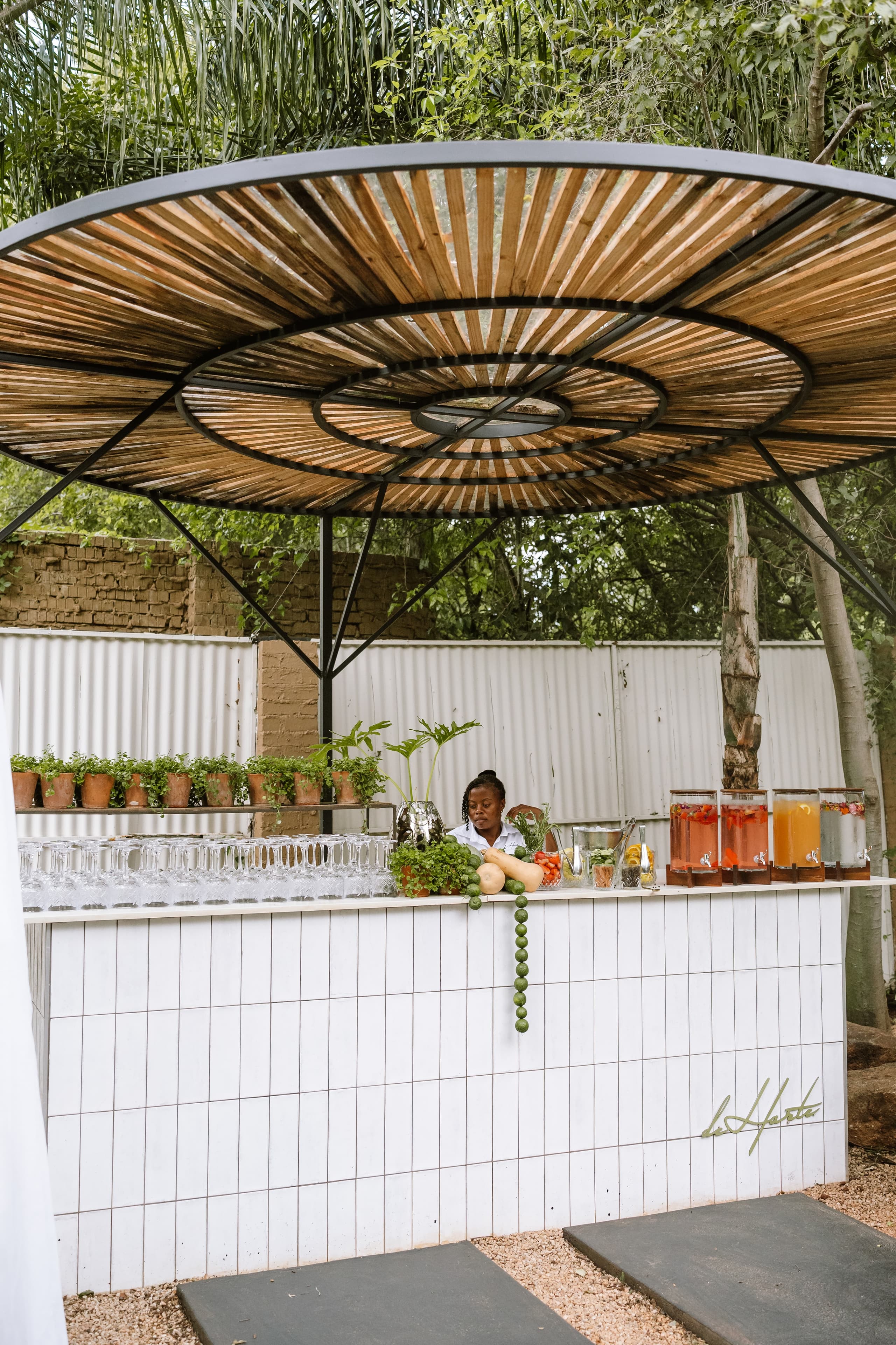 A woman prepares drinks at a modern white tiled bar under a wooden canopy