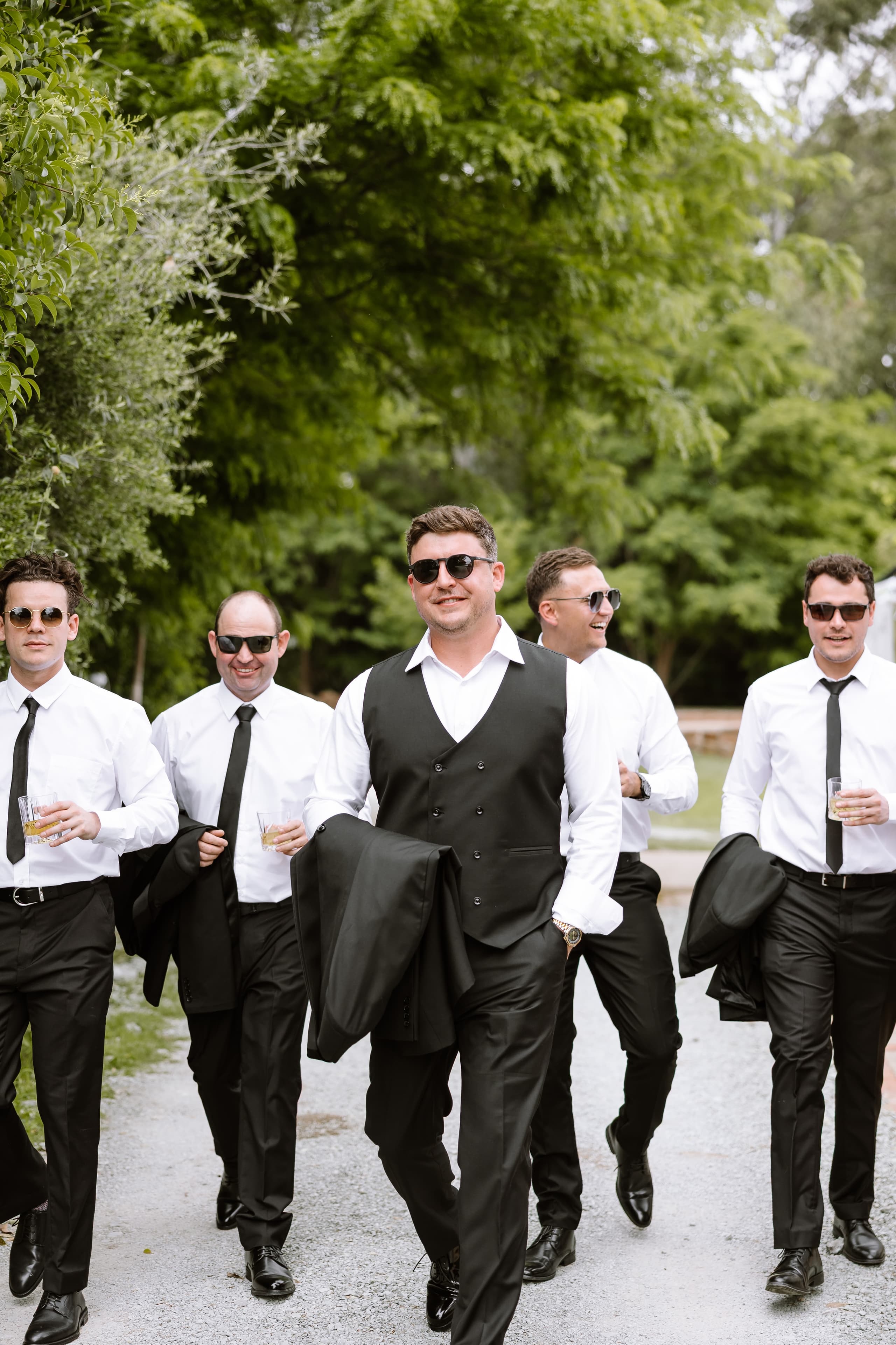 A group of groomsmen in white shirts and black ties walking outdoors while holding jackets