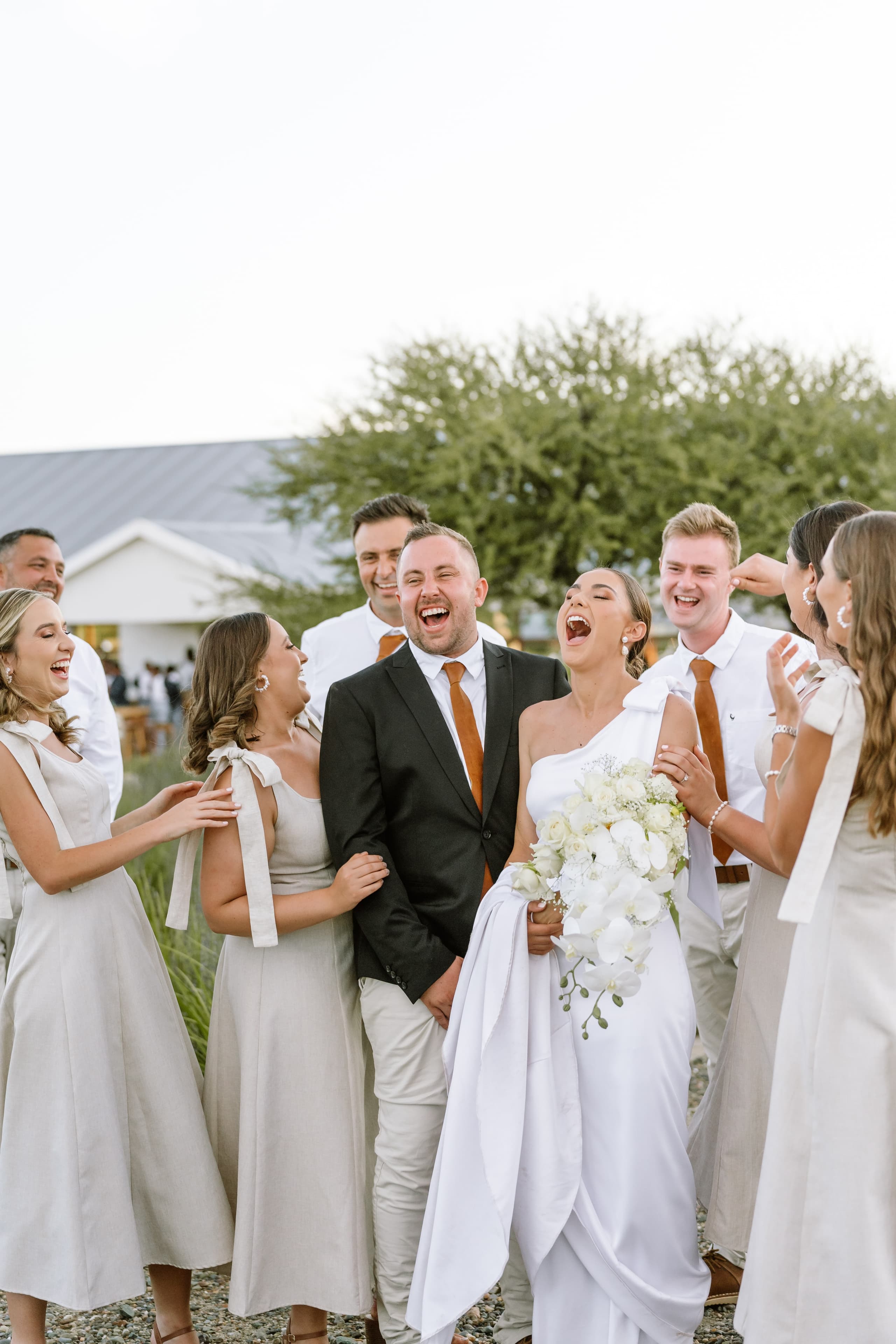 A joyful bride and groom laughing with their bridal party at an outdoor wedding celebration