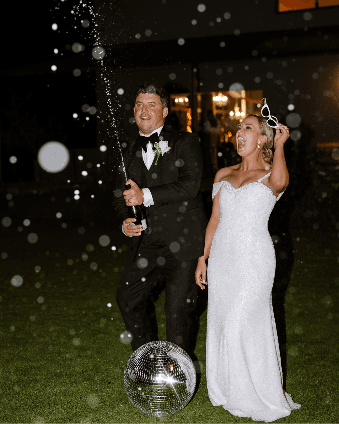 A joyful bride and groom celebrate their wedding night by popping champagne near a disco ball