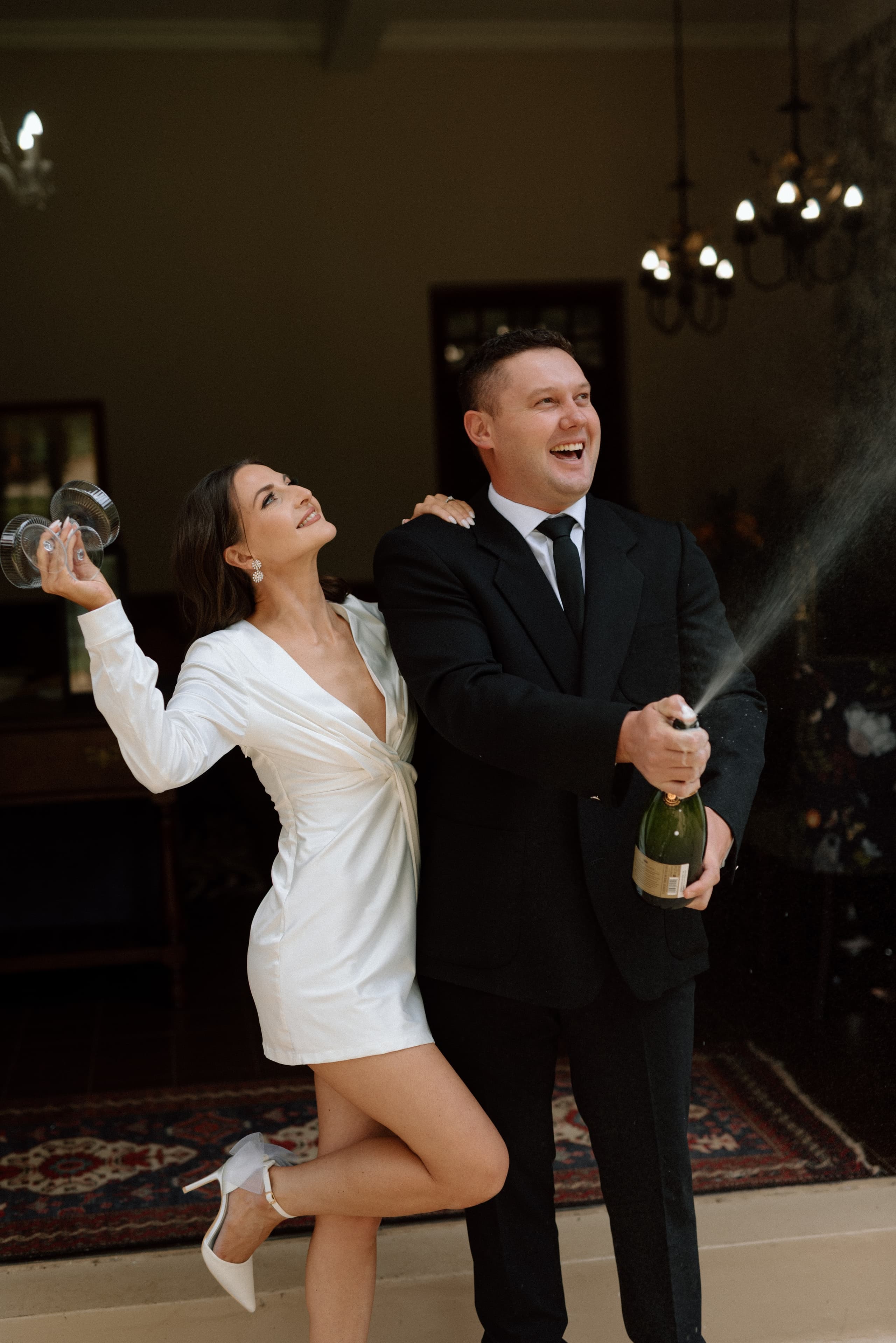 A joyful bride and groom celebrating with a champagne pop at a luxury wedding venue