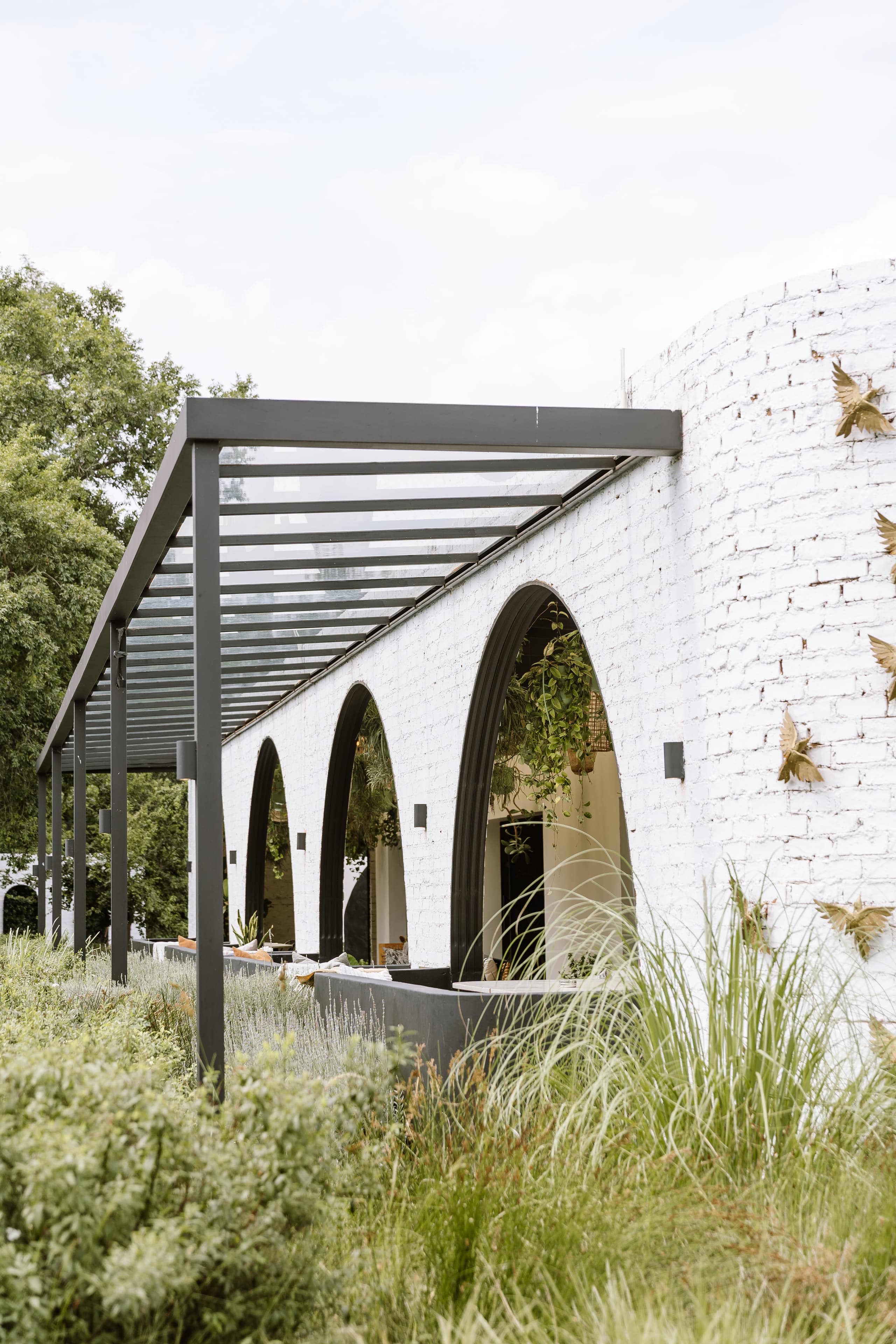 A modern white brick building with arched openings and a sleek black pergola patio structure
