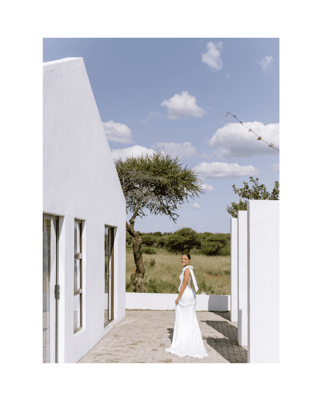 A bride in a white gown smiles while standing on a patio beside modern architecture
