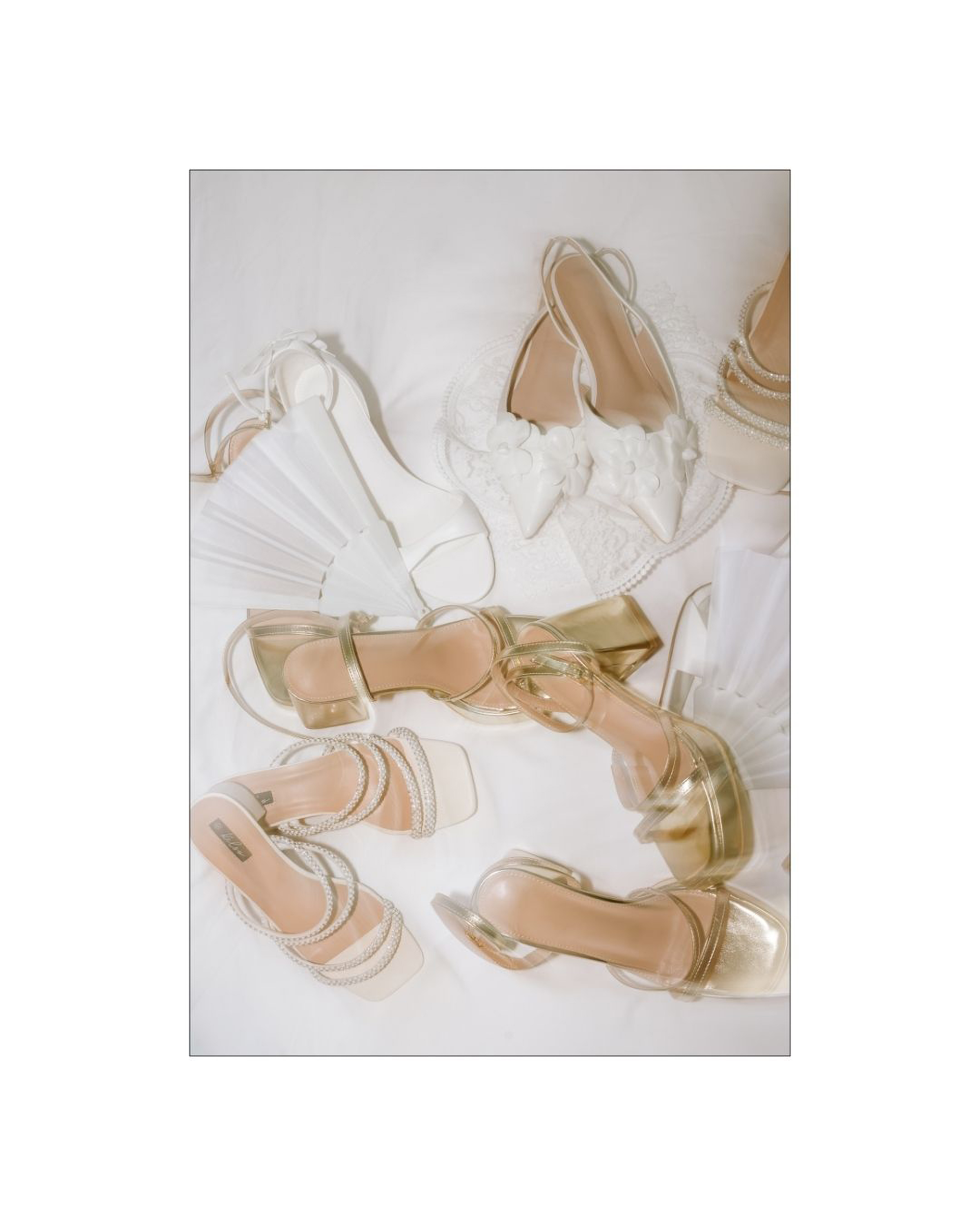 An arrangement of white and gold bridal shoes and folded fans on white fabric