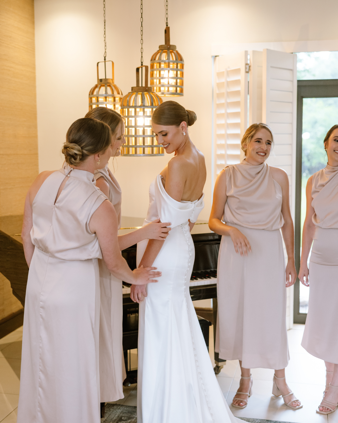 A bride in a white gown stands with her bridesmaids in champagne dresses indoors