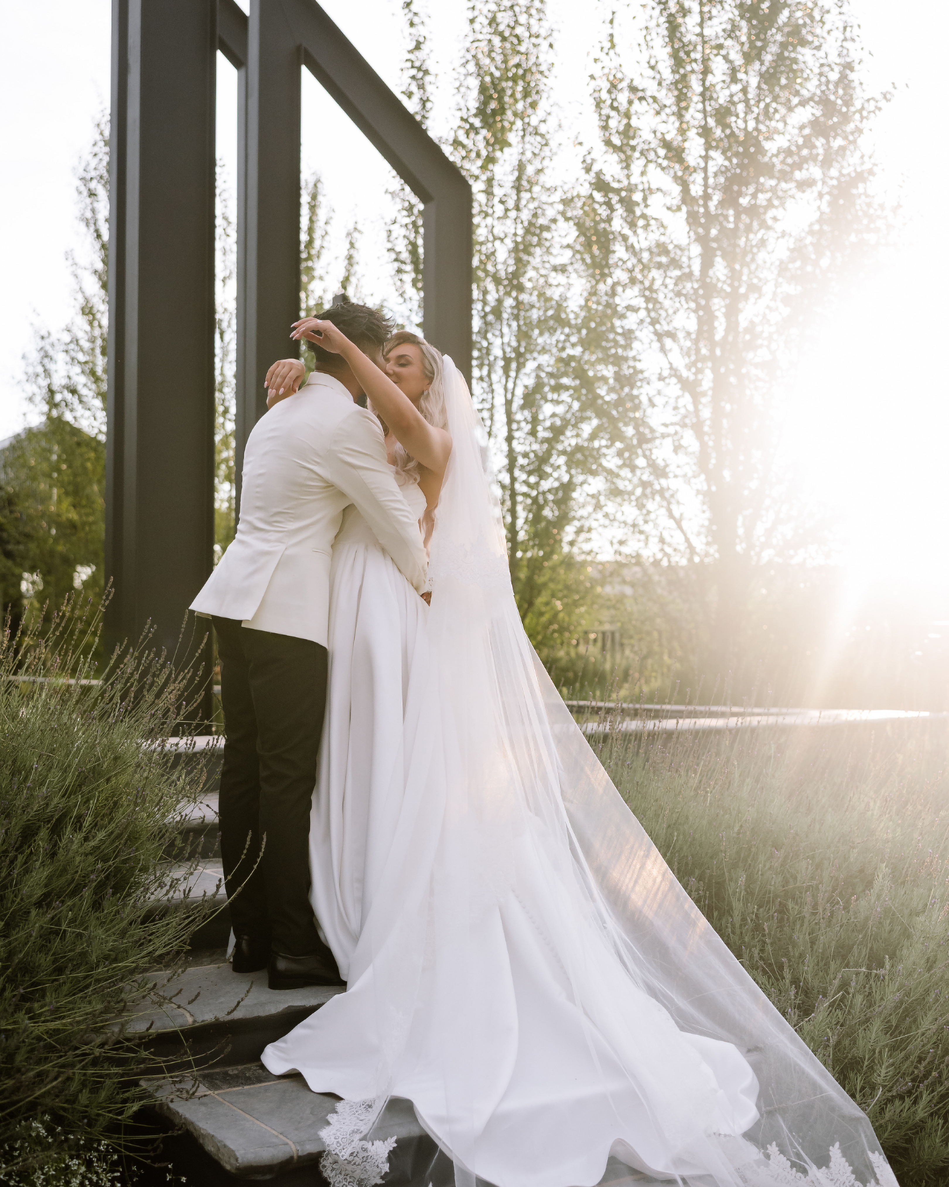 A bride and groom share an intimate embrace on stone steps at sunset outdoors