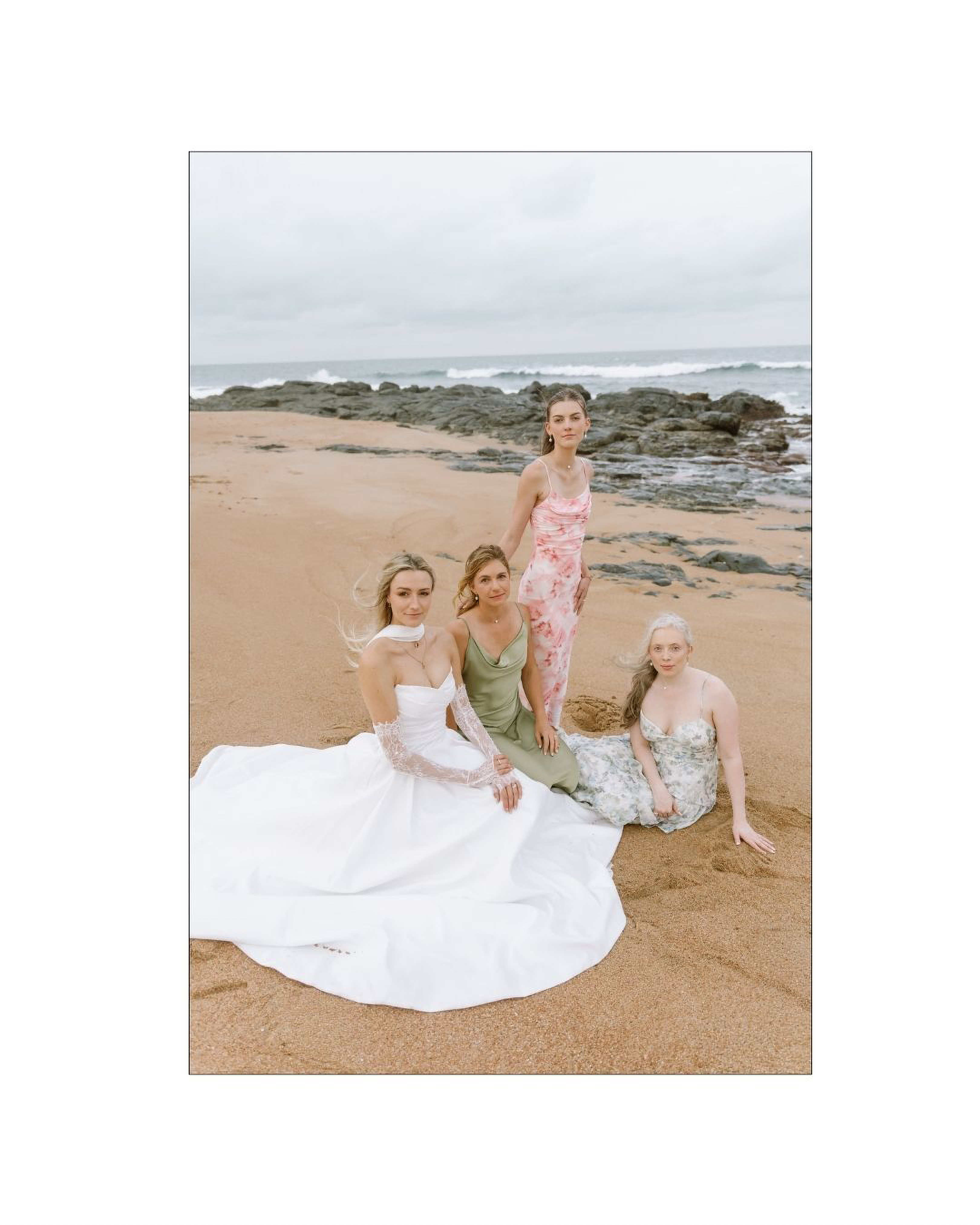 A bride in a white gown and her bridesmaids on a sandy beach
