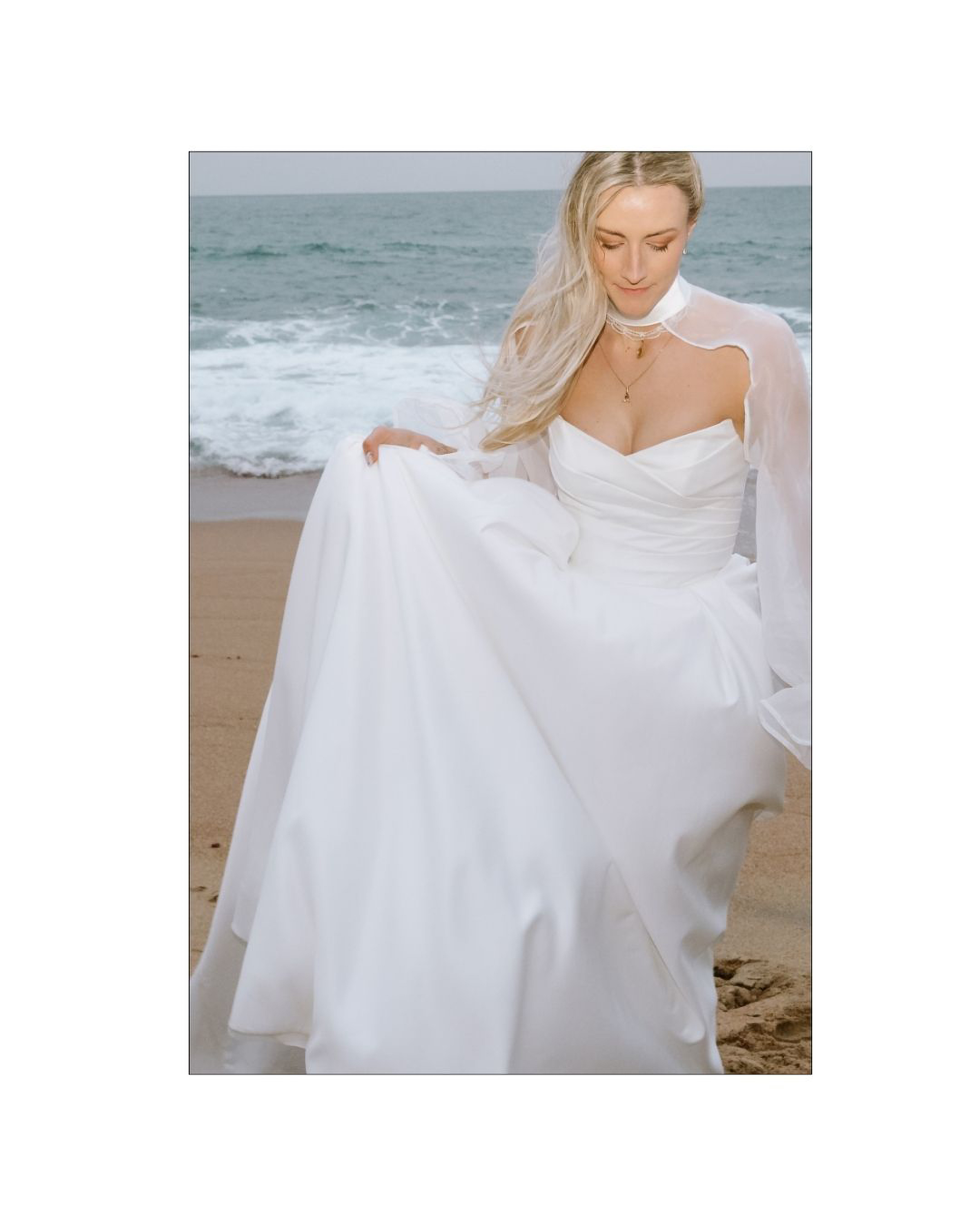 A bride in a white gown holding her dress on a beach
