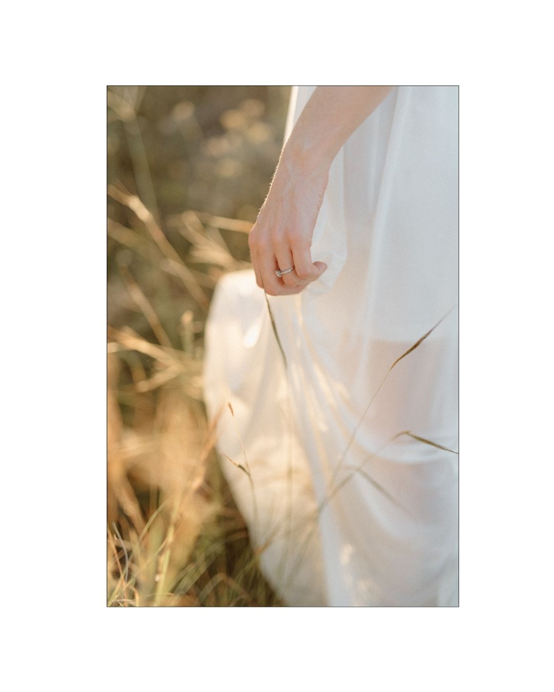 A bride wearing a diamond ring gently holds the fabric of her white wedding dress