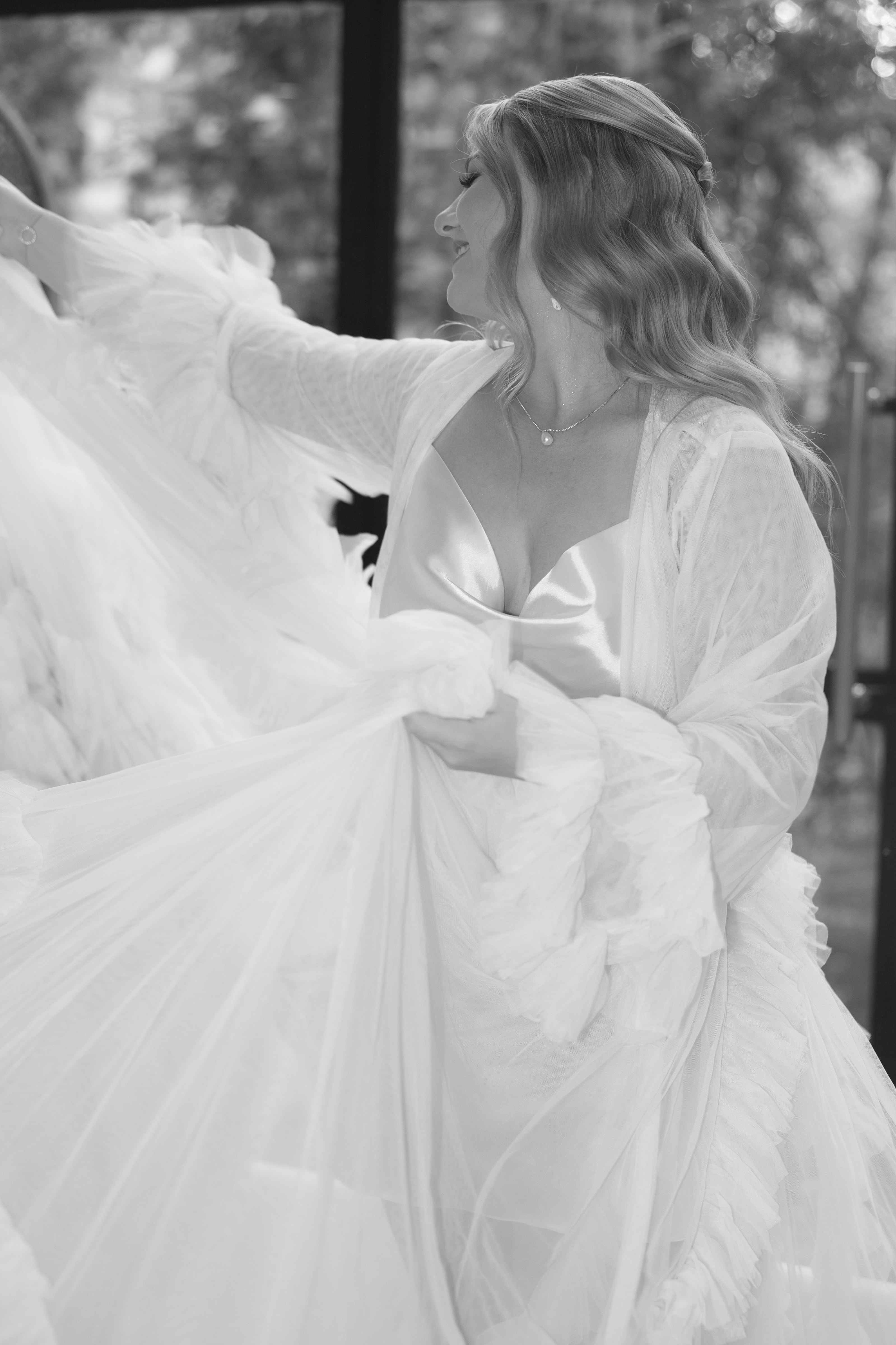 A bride in a satin slip dress and ruffled tulle robe smiles while posing