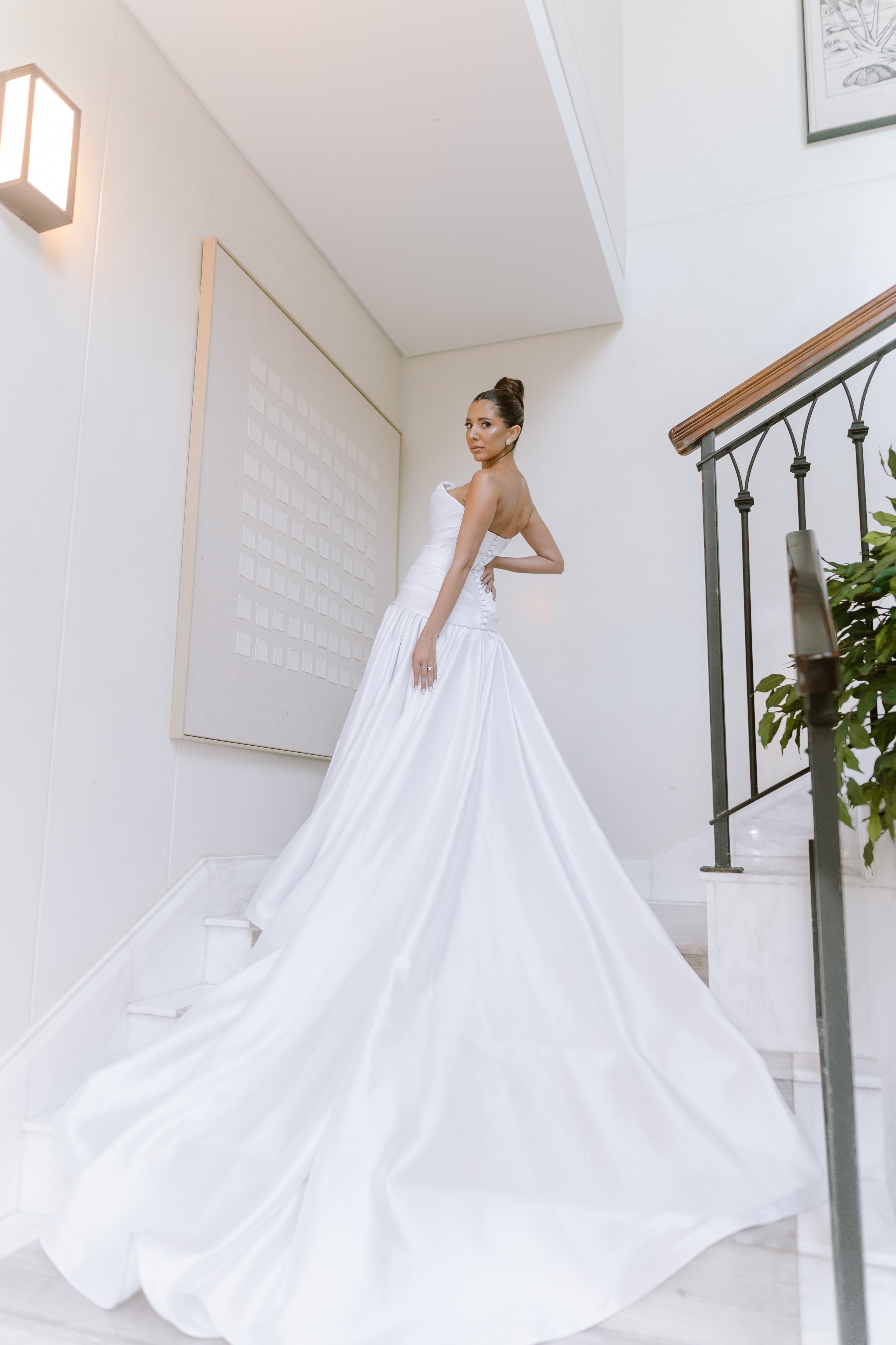 A bride in a strapless white gown poses elegantly on a modern marble staircase