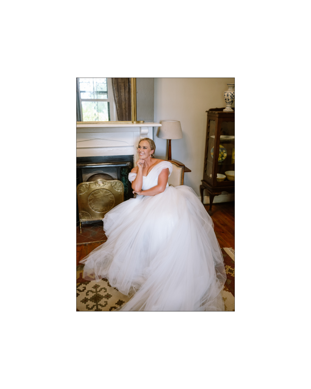 A smiling bride in a voluminous white tulle gown sits gracefully in an elegant room