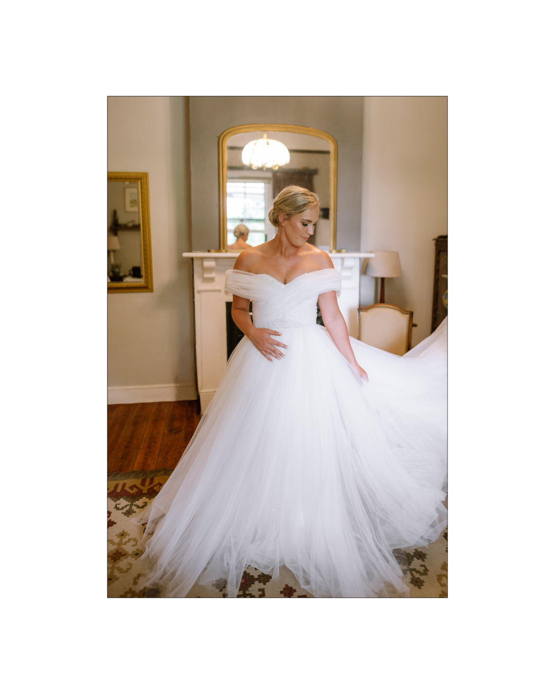 A radiant bride in an off-the-shoulder tulle wedding gown stands inside a historic room