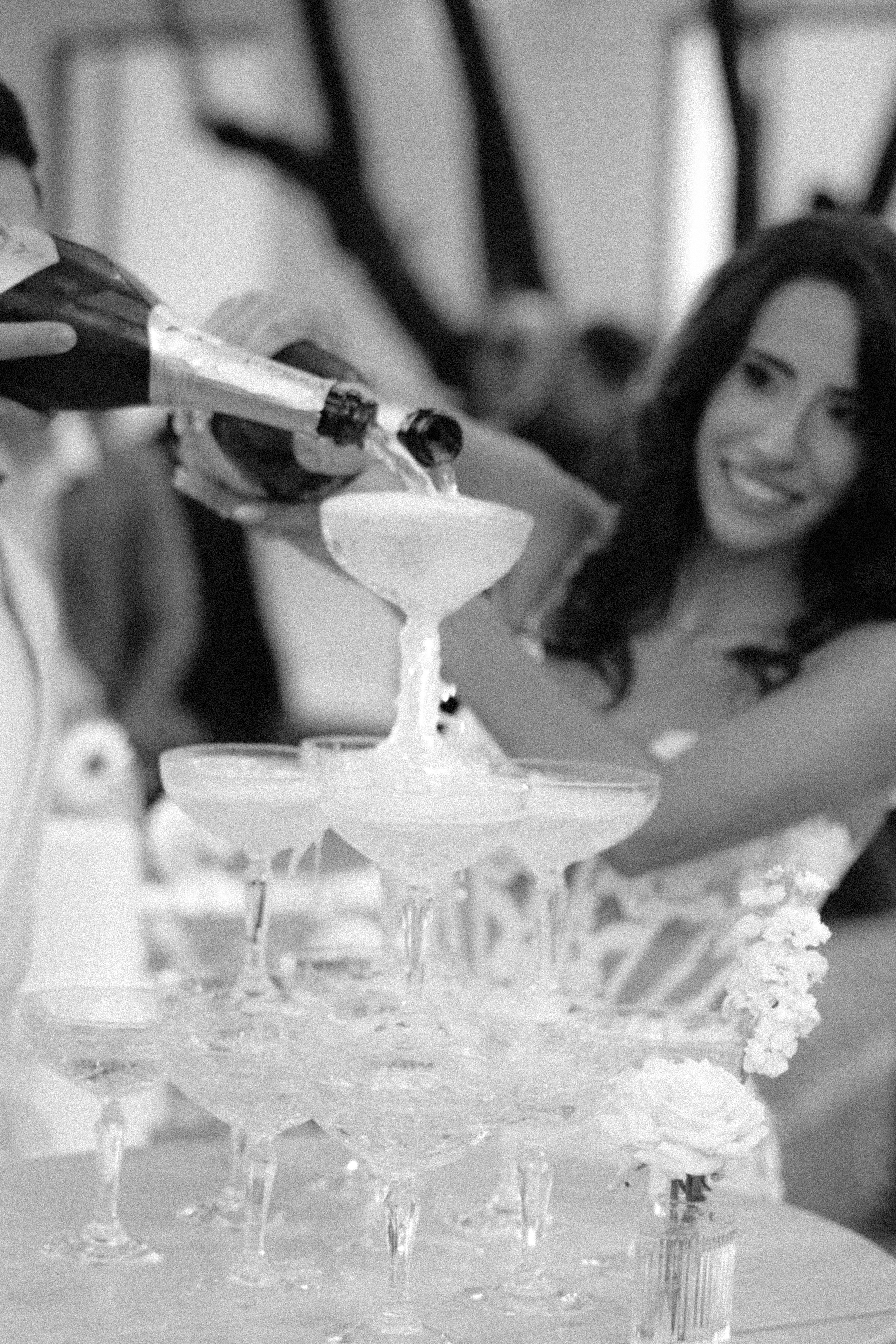 A bride smiles as champagne is poured into a tiered crystal coupe glass tower