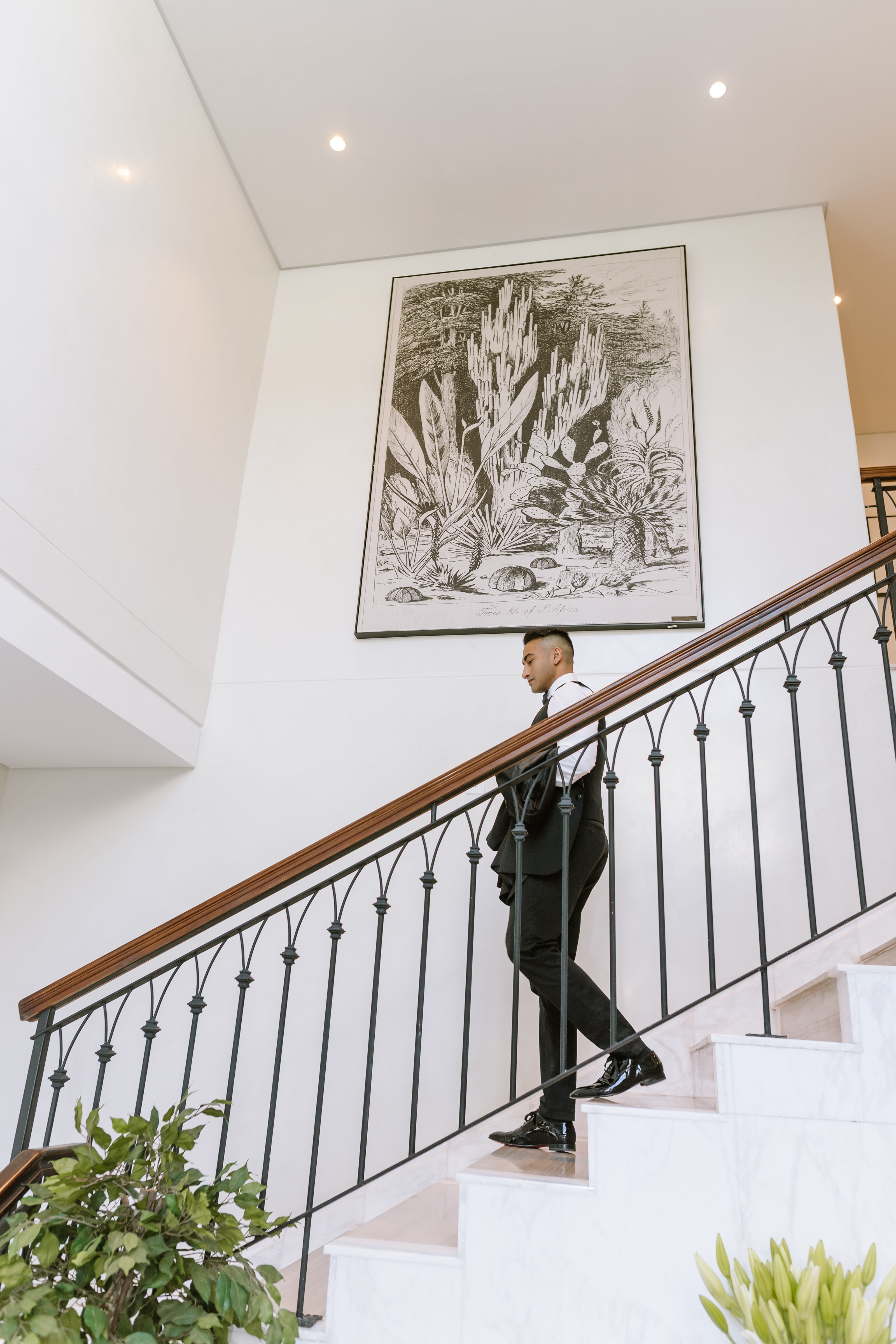 A stylish man in a formal suit walks down a grand marble staircase indoors
