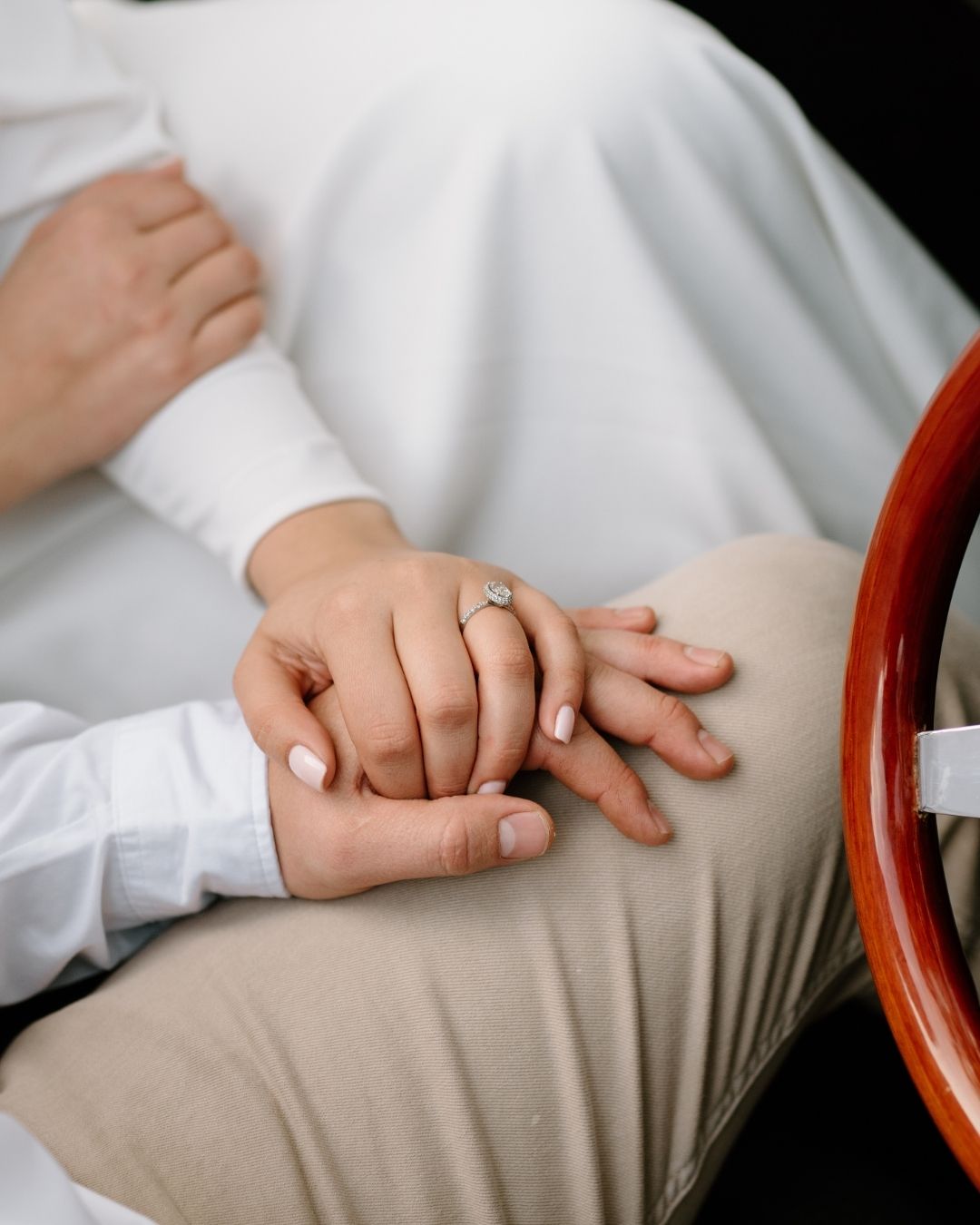 A bride and groom hold hands gently while sitting inside a vintage luxury car