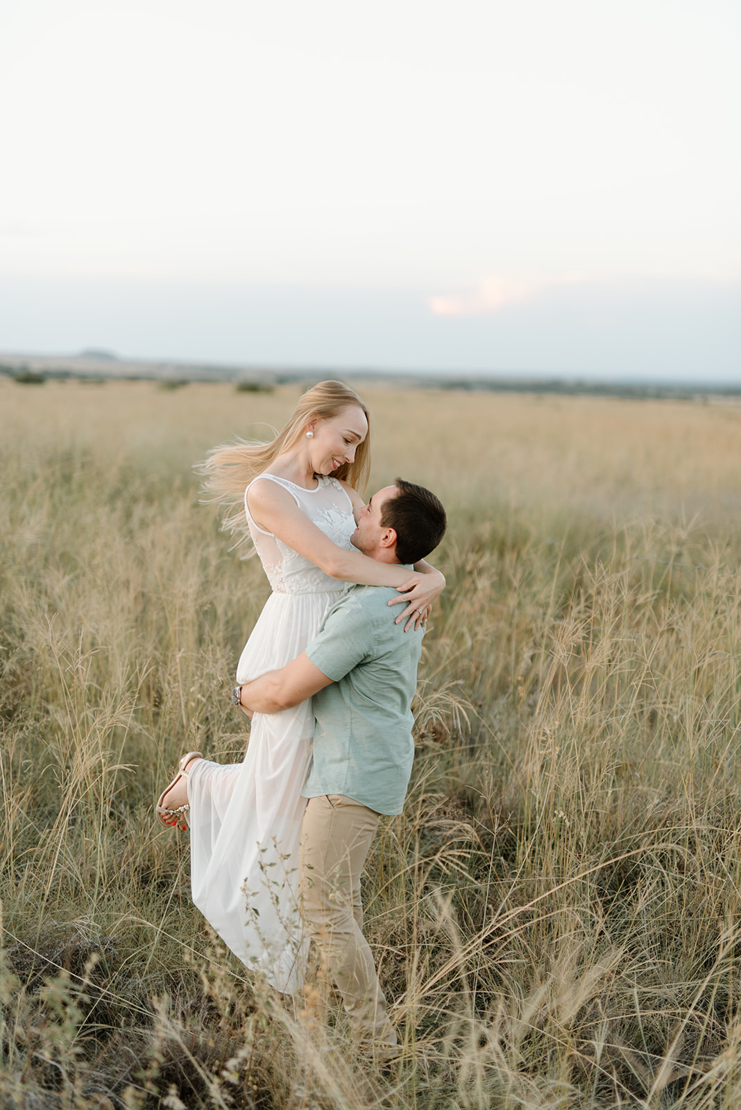 A man lifts his smiling partner in a golden grassy field at sunset