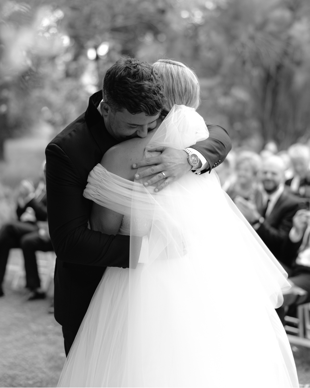 A groom embraces his bride in a heartfelt hug during their outdoor wedding ceremony