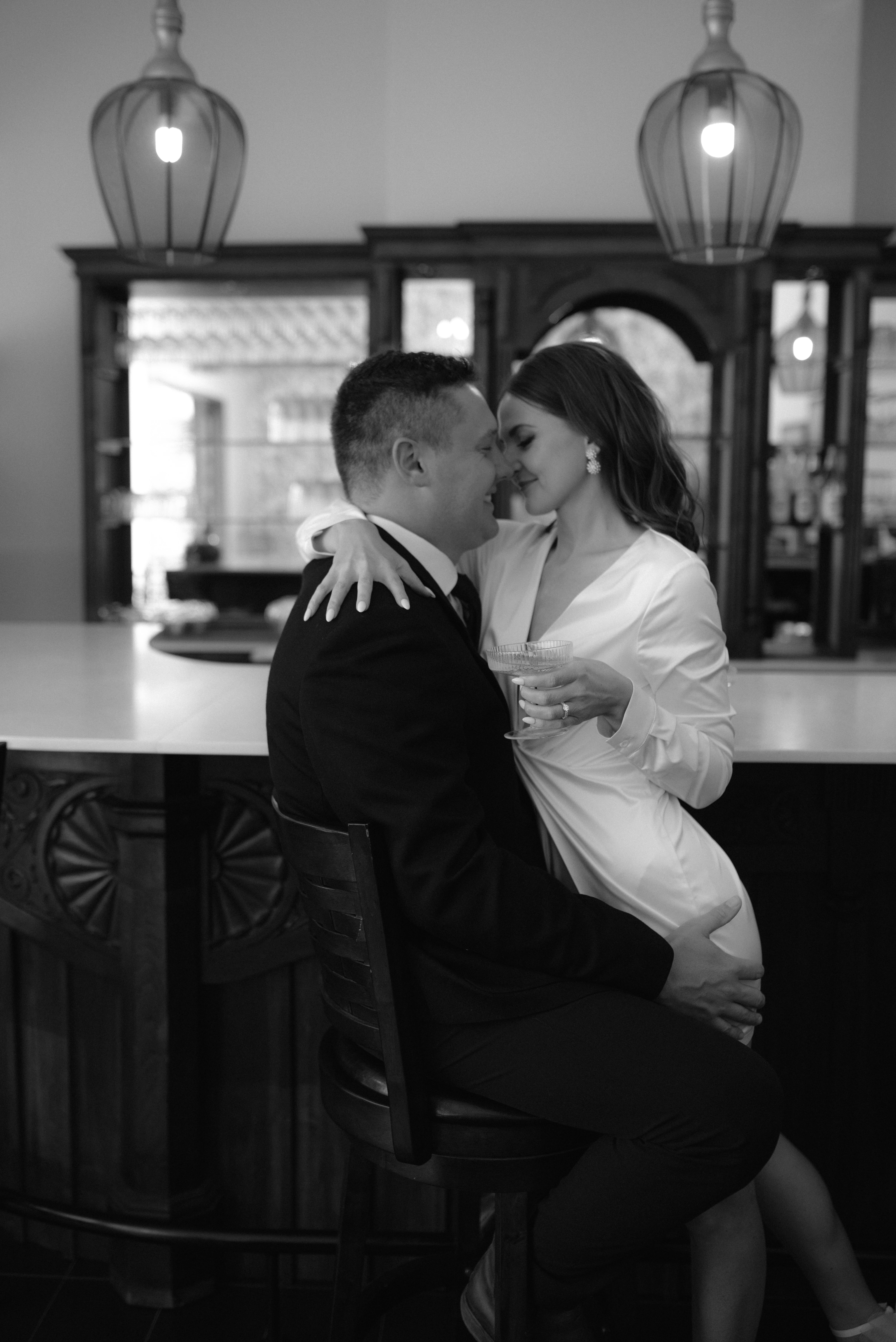 A newlywed couple shares an intimate moment while sitting at a sophisticated wooden bar
