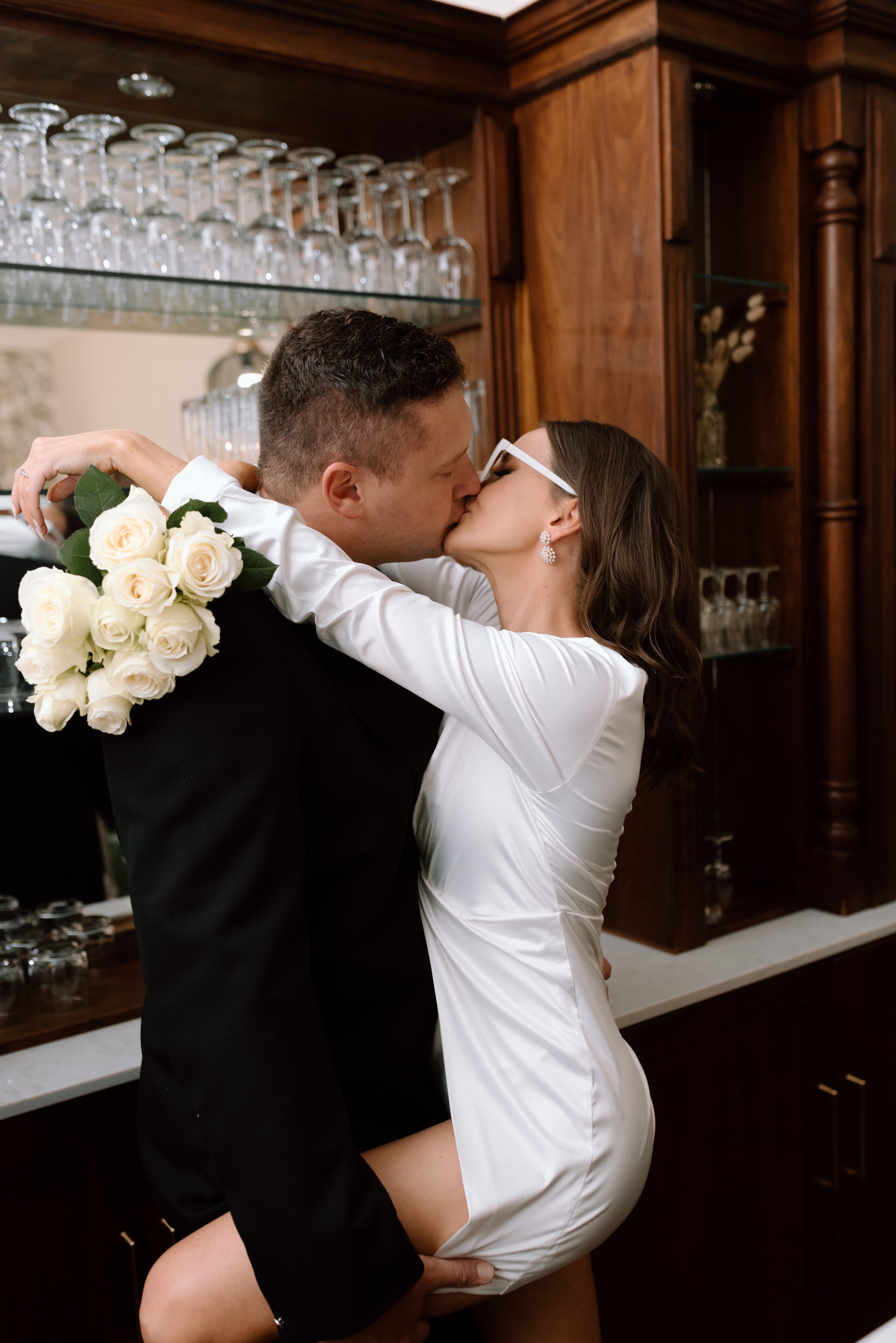 A bride and groom share an intimate kiss while standing at a wooden bar counter