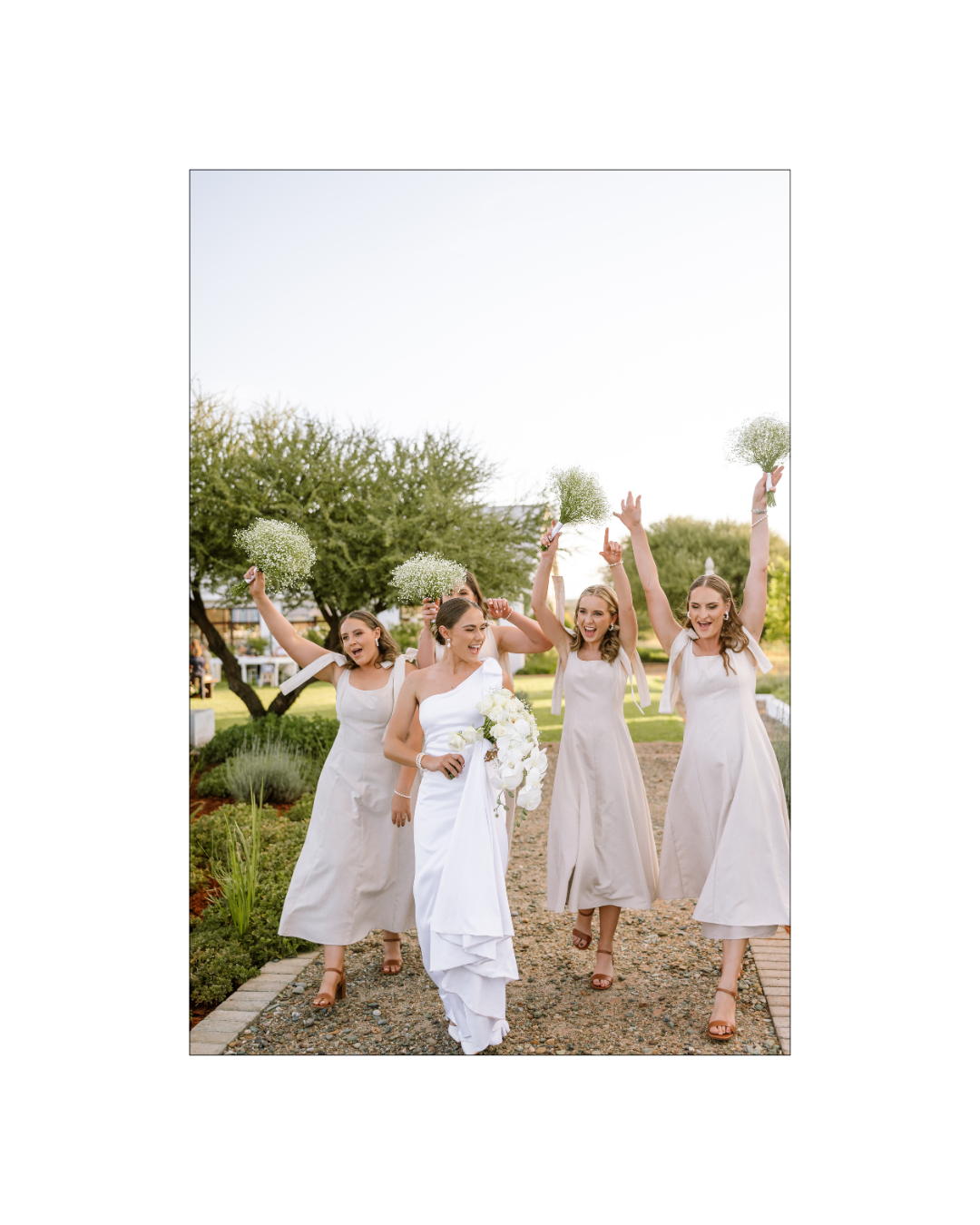 A joyful bride and her four bridesmaids walking outdoors while holding baby's breath bouquets