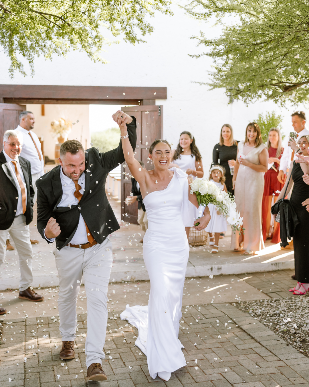 A joyful bride and groom walk hand in hand through confetti after their wedding ceremony