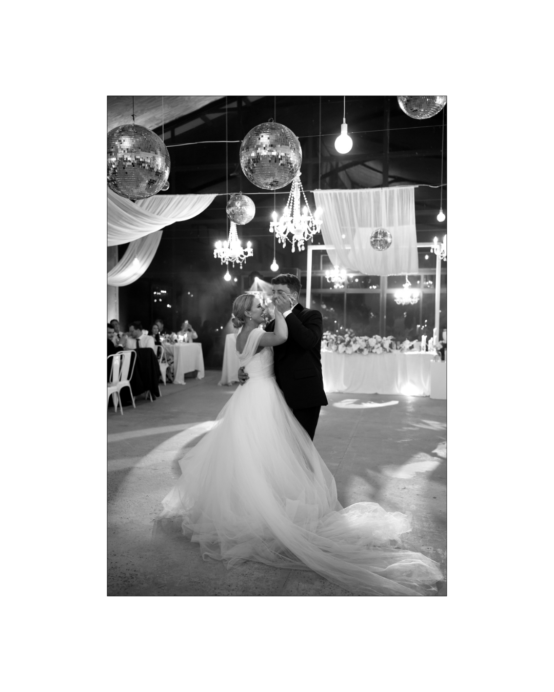 A bride and groom share an intimate first dance under hanging disco balls and chandeliers