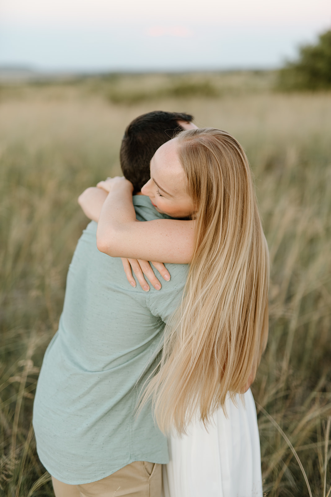 A blonde woman embraces her partner in a golden field during a romantic sunset session