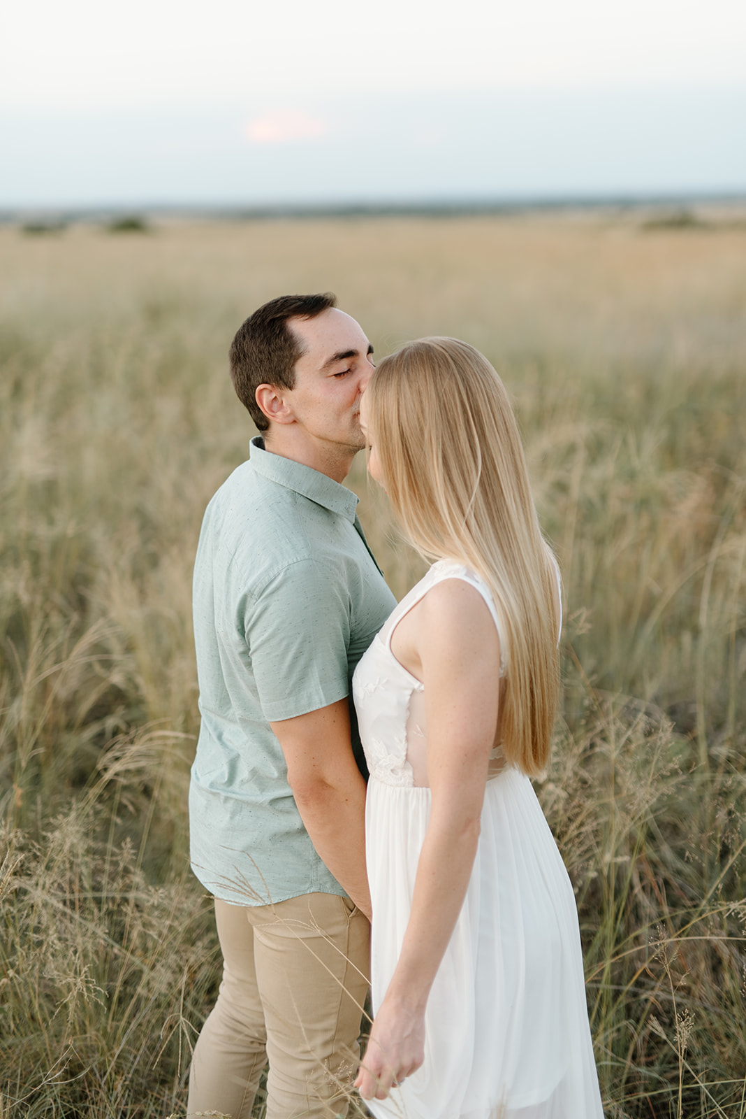 A couple shares a tender moment while standing in a vast, sun-drenched grassy field