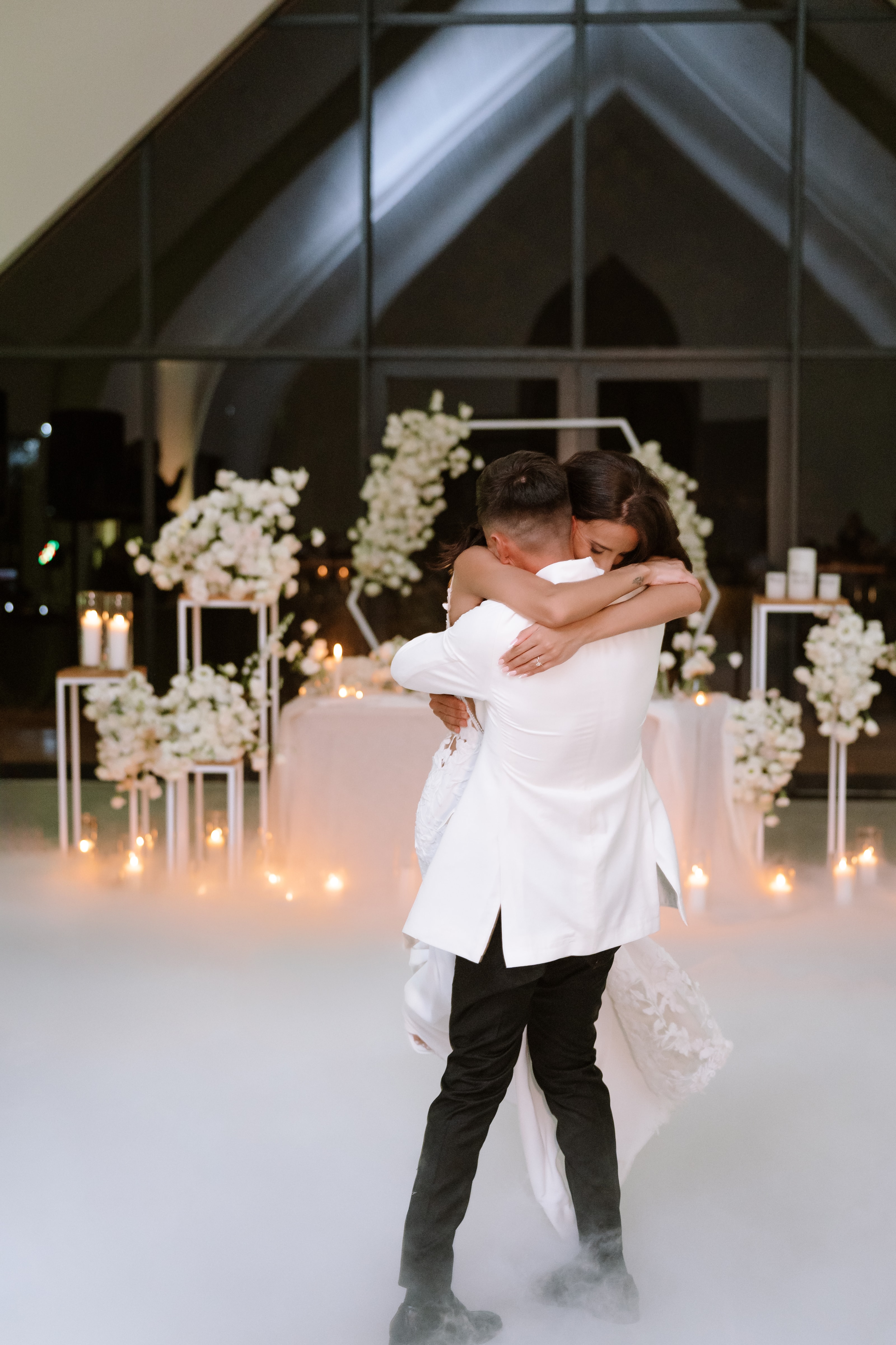 A newlywed couple shares a romantic embrace on a dance floor filled with low-lying fog