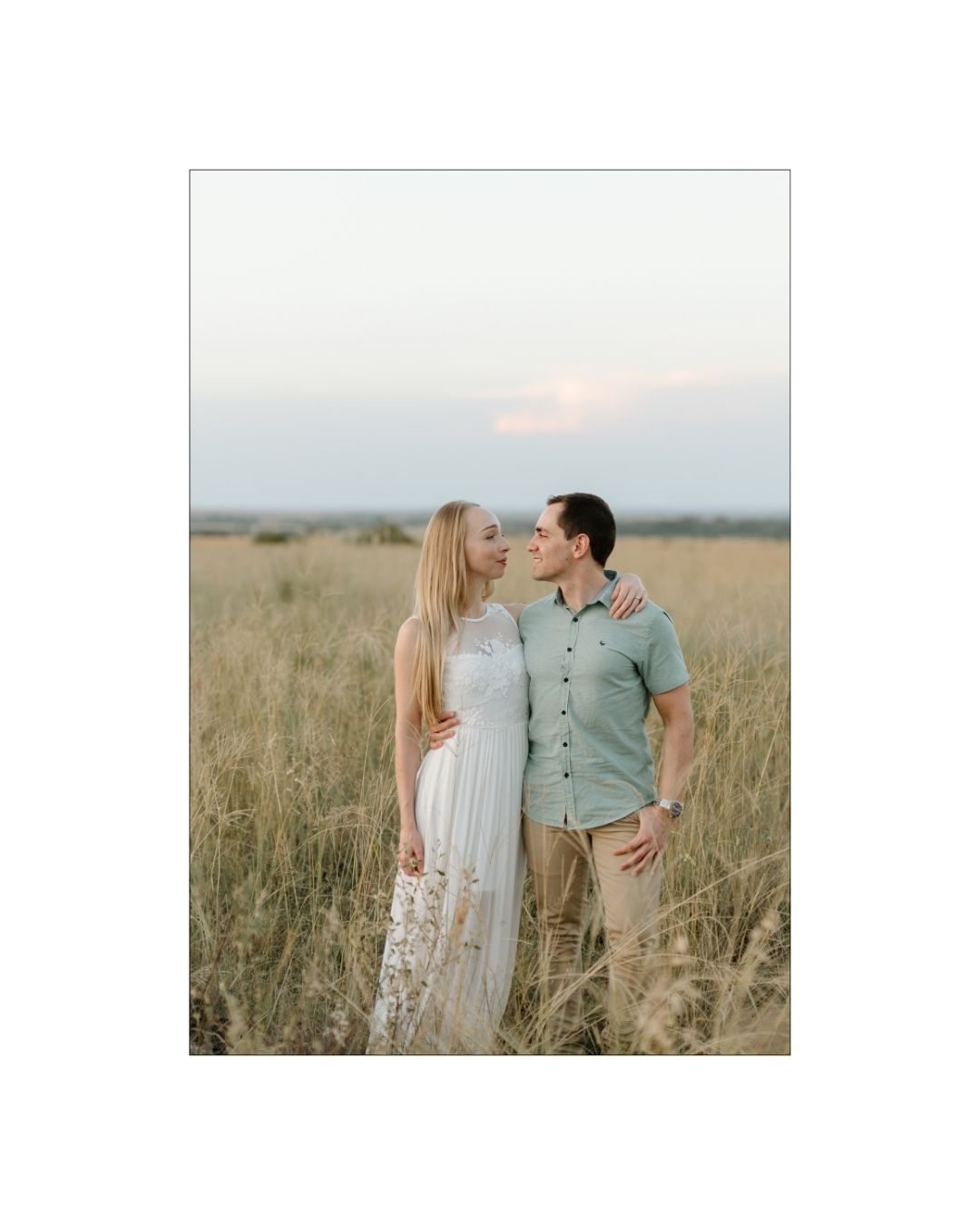 A romantic couple stands in a golden South African field during a soft sunset