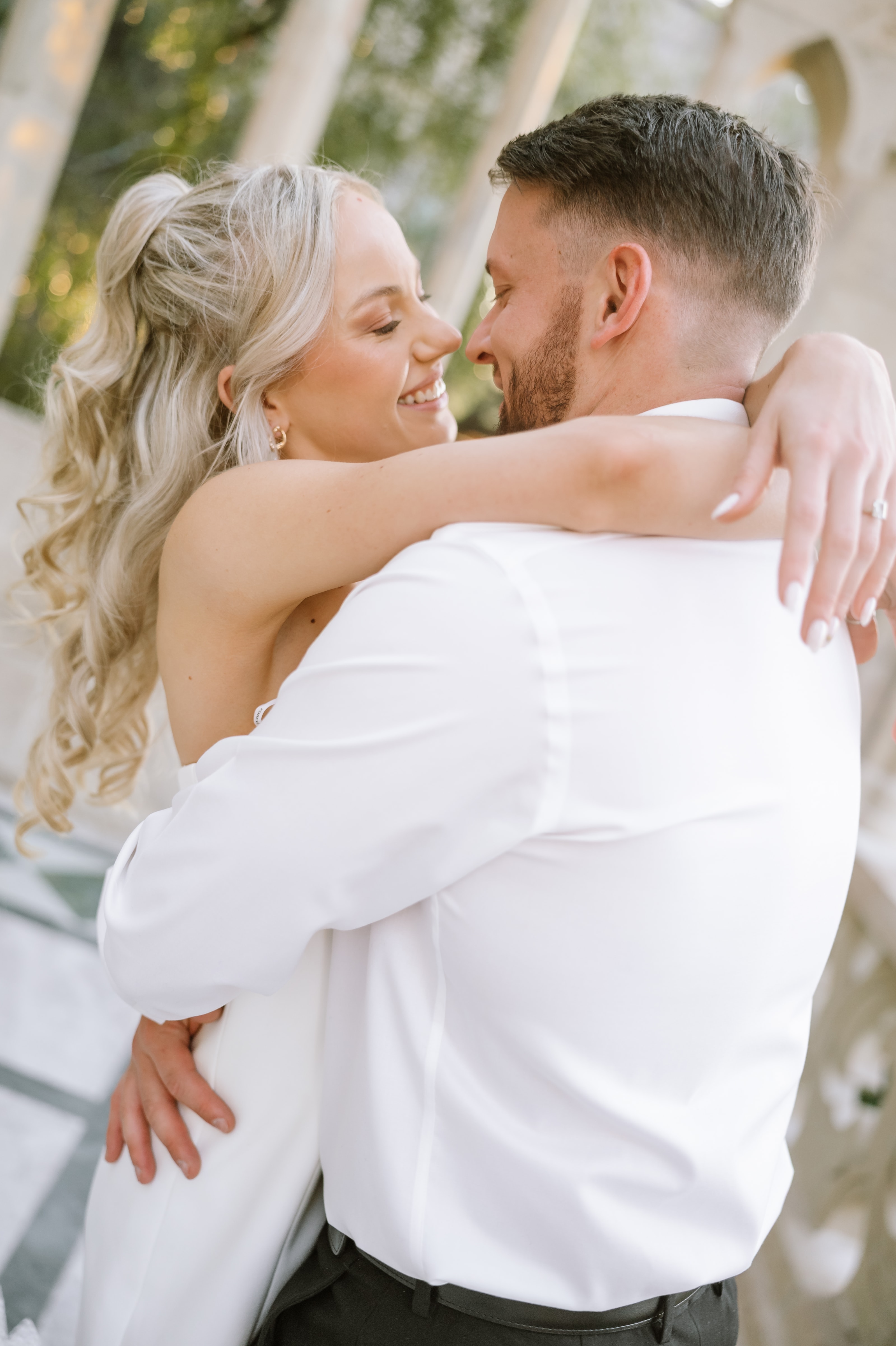 A smiling blonde bride embraces her groom during a romantic outdoor sunset wedding portrait session