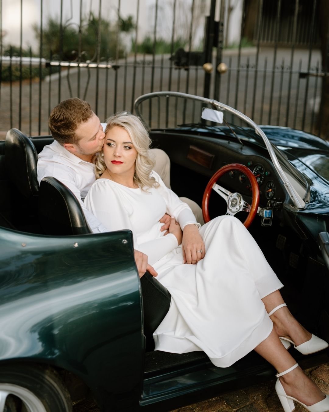 A romantic couple in wedding attire embracing inside a vintage dark green convertible car
