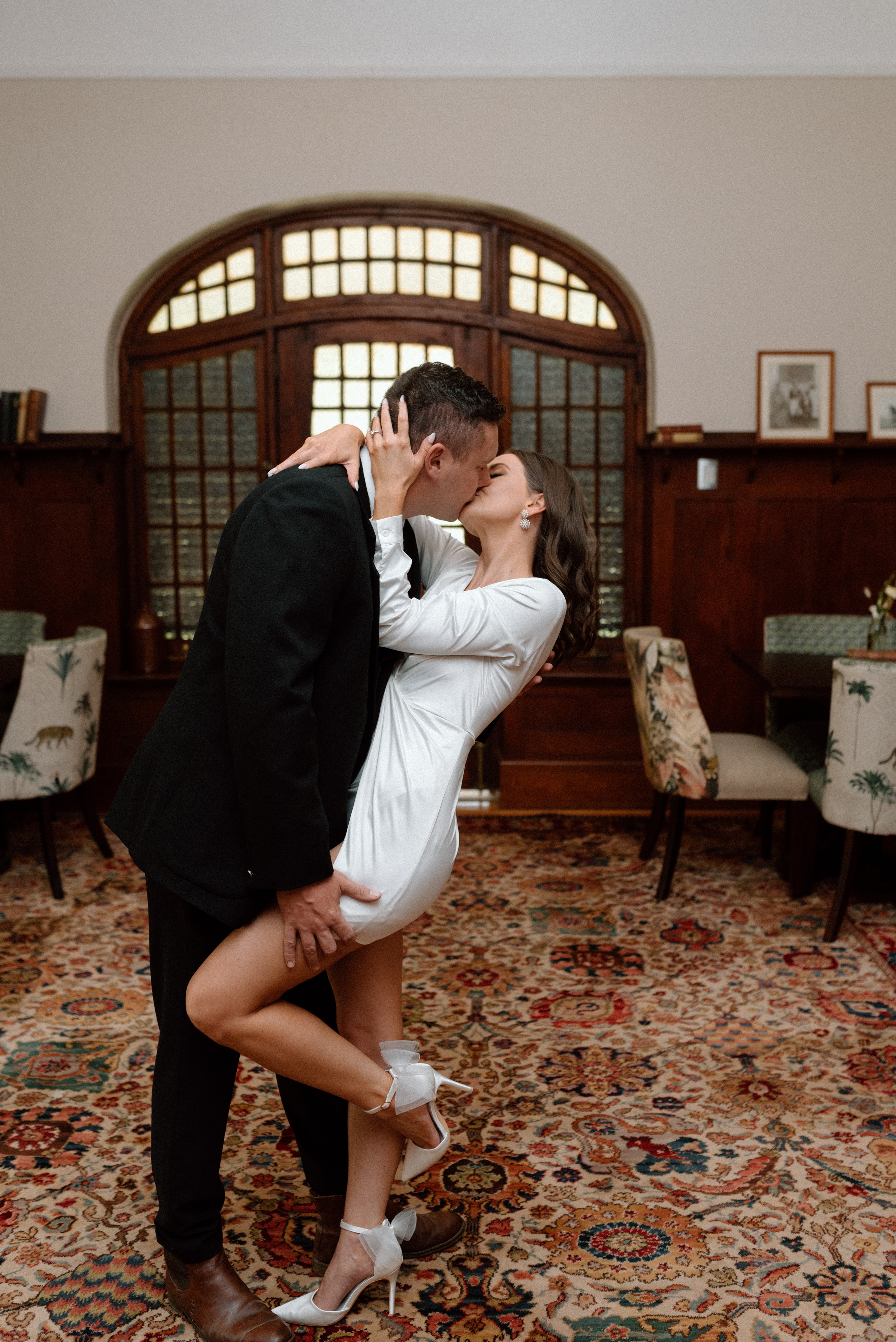 A newlywed couple shares a romantic kiss while dipping in a wood-paneled historic room