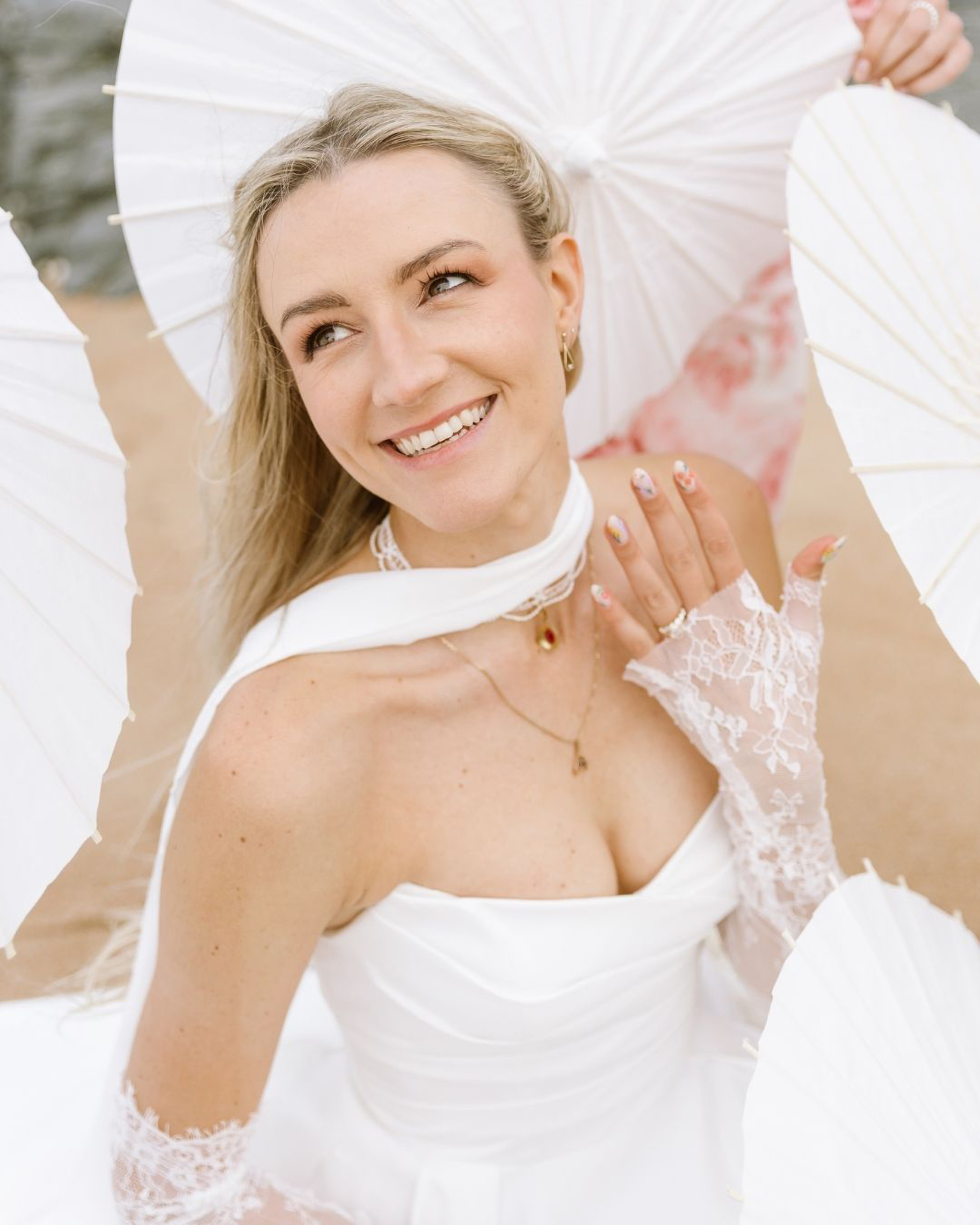 A smiling bride wearing white lace gloves holds several traditional paper umbrellas